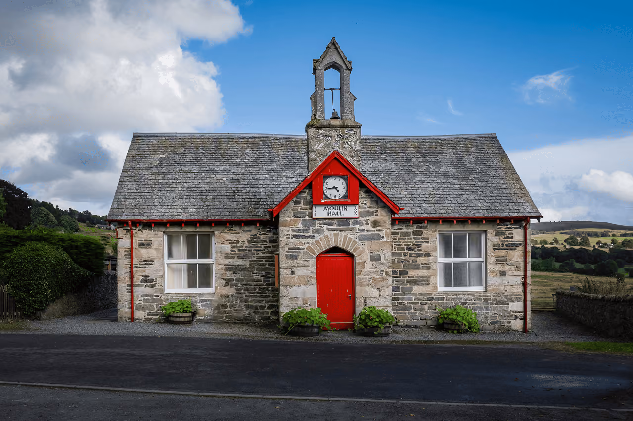 Moulin Hall historic stone building with a bright red door and clock tower set against rolling Scottish countryside