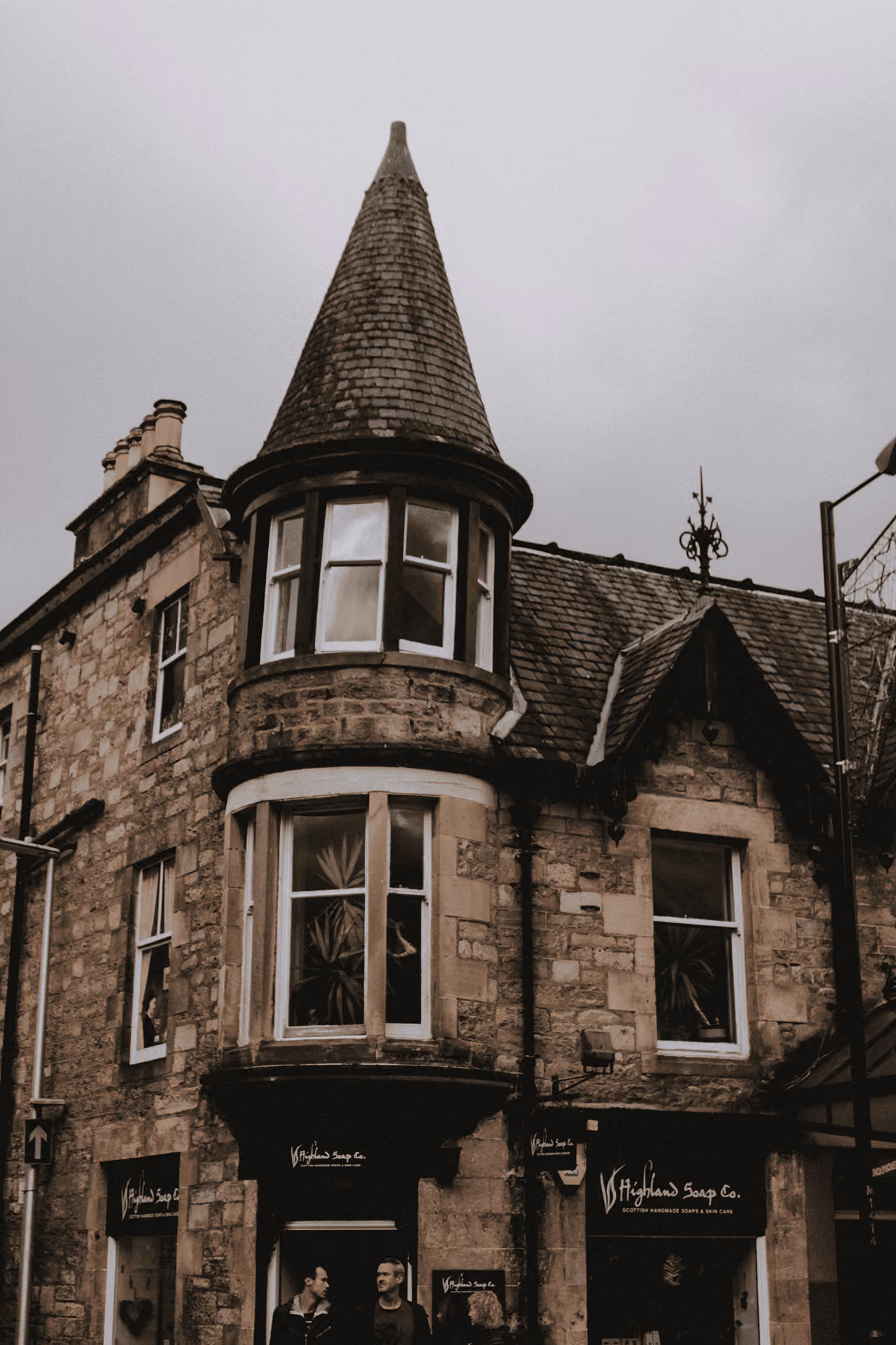 A turreted Victorian sandstone corner building housing the Highland Soap Company shop on a Pitlochry street