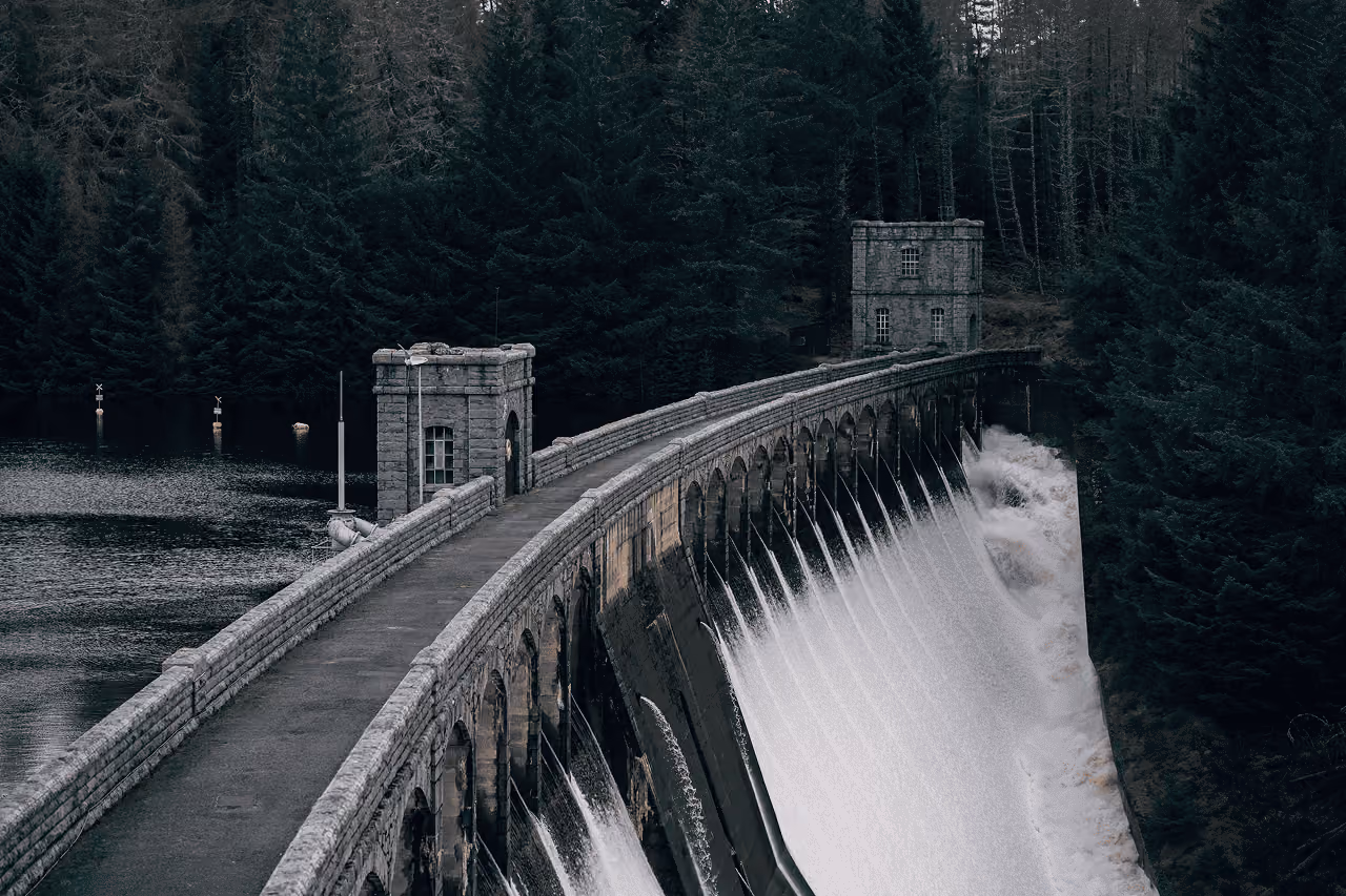 Pitlochry Dam curving across the River Tummel with water flowing through the sluice gates and forested hills rising behind