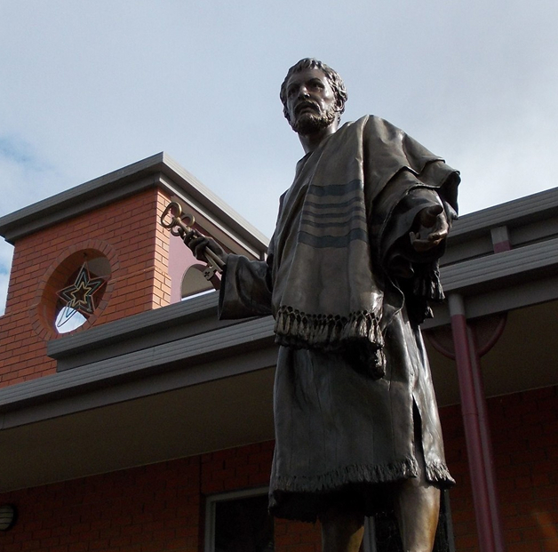 Bronze statue of a bearded man holding large keys in front of a building with a brick arch.
