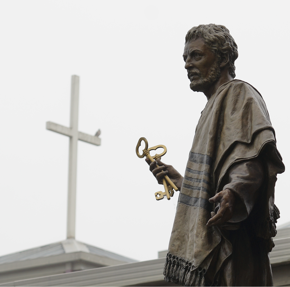 Bronze statue of a bearded man holding large keys in front of a building with a brick arch.