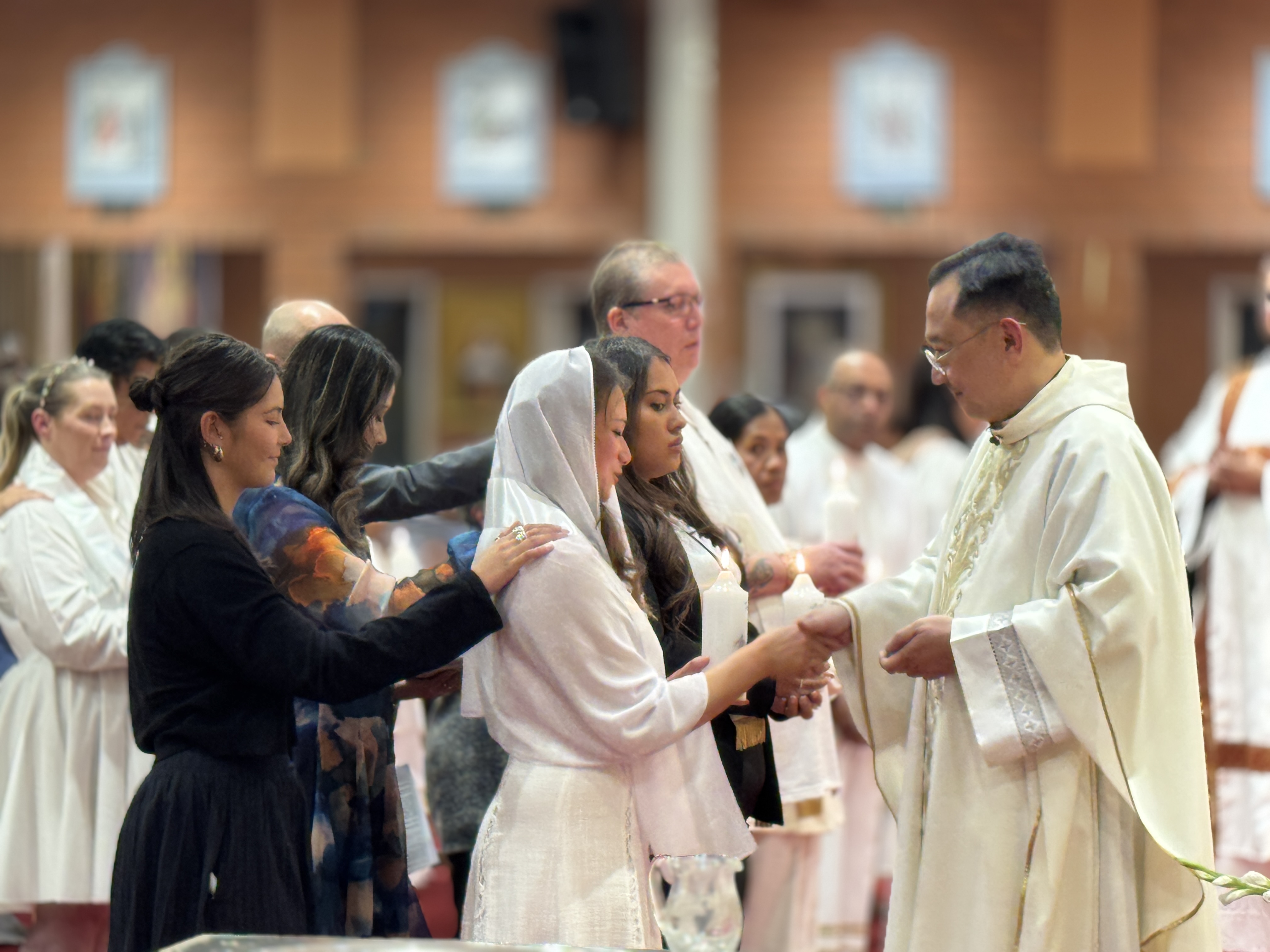 Priest raising a chalice at church altar during a religious ceremony with stained glass windows.
