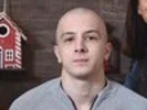 Real client - 2: Young bald man wearing a grey shirt sitting indoors with a birdhouse visible in the background.