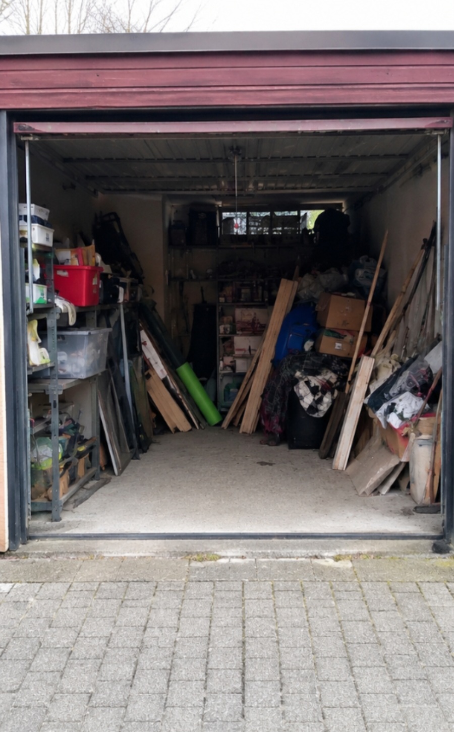 Open garage filled with various tools, boxes, wooden planks, and storage shelves on both sides.