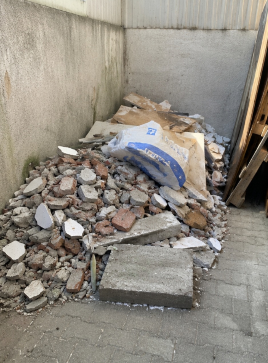 Pile of broken concrete, bricks, and construction debris inside a narrow, walled outdoor space.