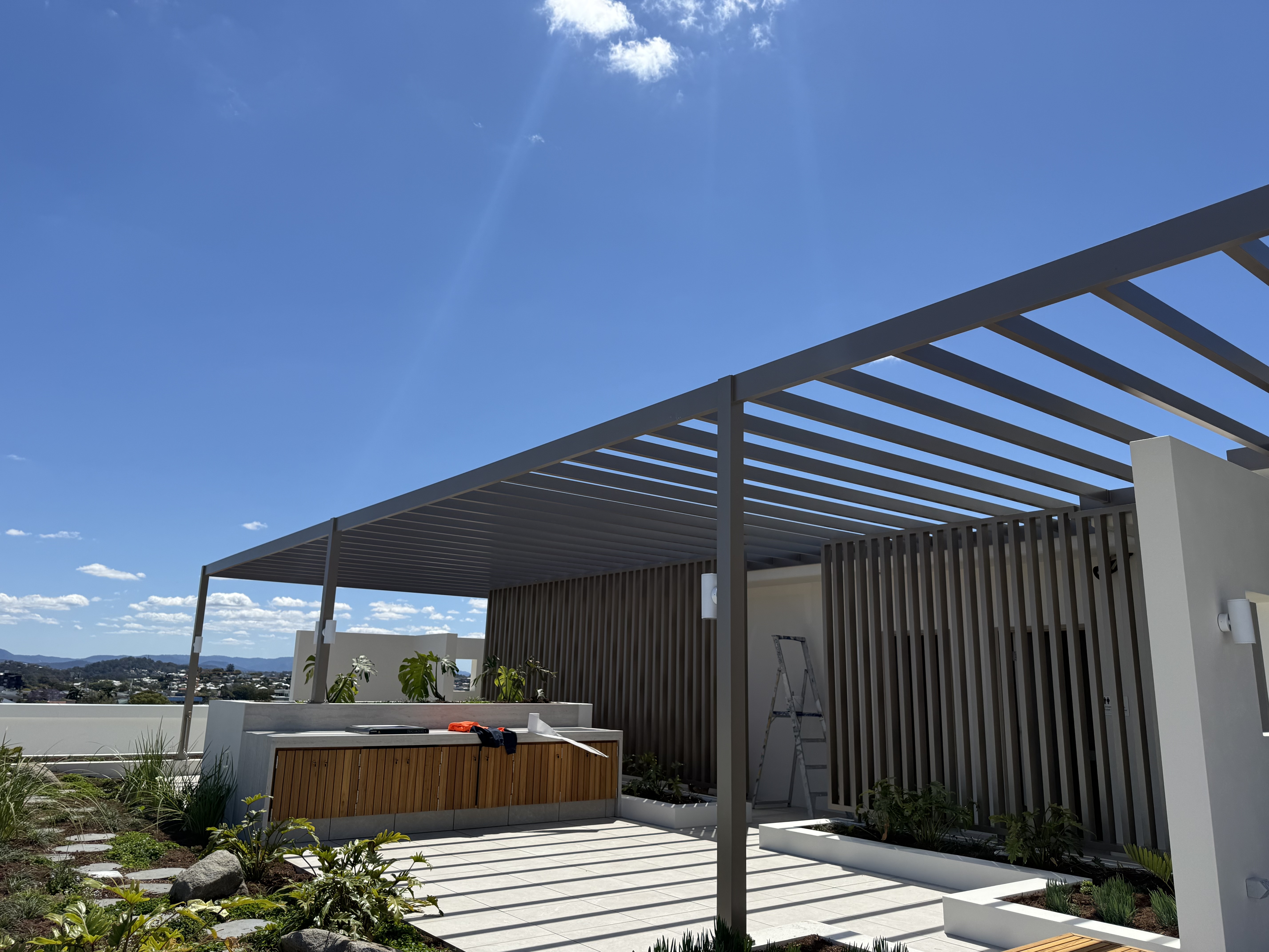 Rooftop communal terrace with aluminium pergola and batten screens, district views beyond