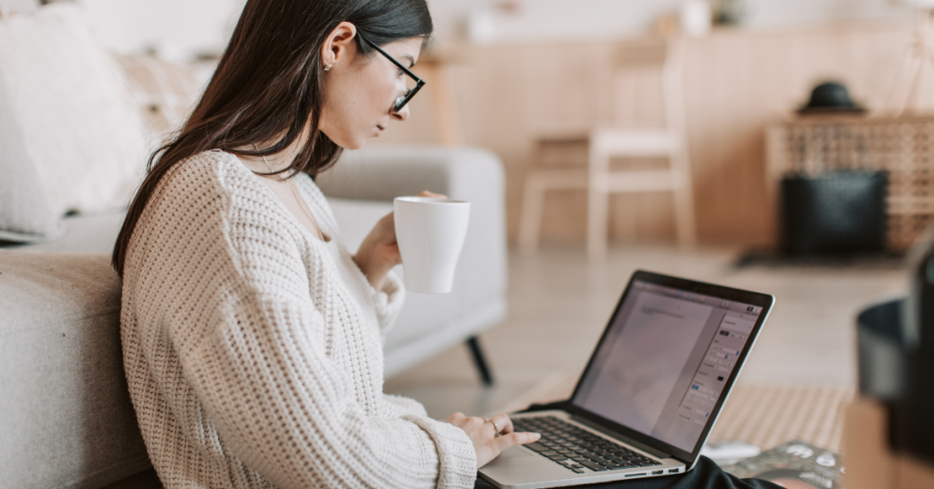 Implications for Businesses and Content Creators | A woman holding a cup of coffee working on her laptop.