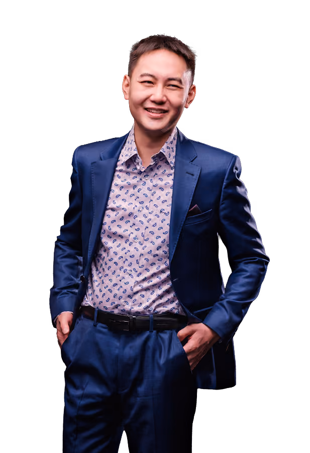 Smiling man in a blue suit with hands in pockets, wearing a patterned shirt against a black background.
