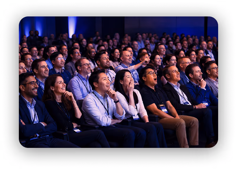 Large diverse audience seated indoors attentively watching and reacting positively at an event or presentation.