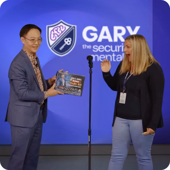 Man in suit hands a boxed product to excited woman in front of a purple backdrop with a security logo.