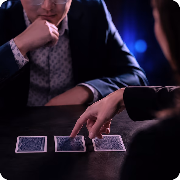 A person pointing to one of three face-down playing cards during a card game or magic trick.