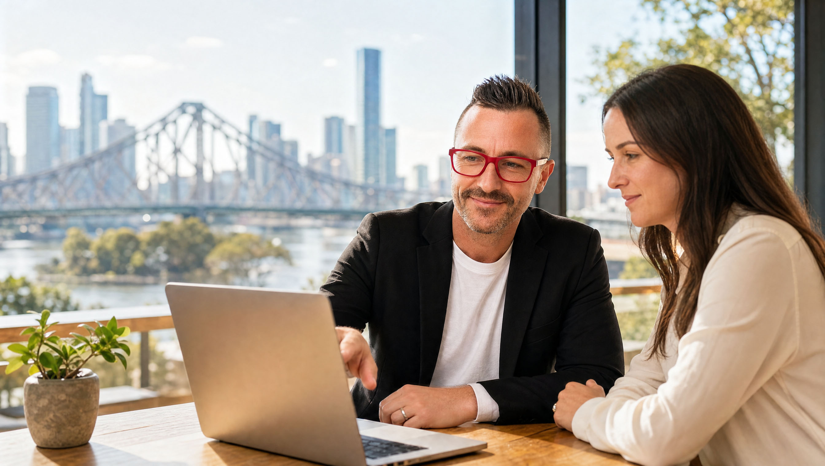 Two people working with AI on a laptop, Story Bridge Brisbane behind