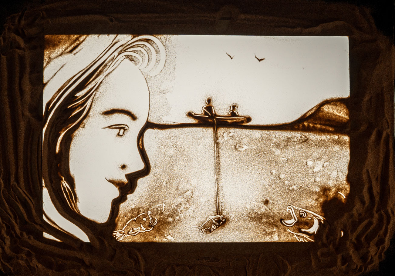 Sand art showing a large face, two people in boat, fishing line, and three fish underwater.