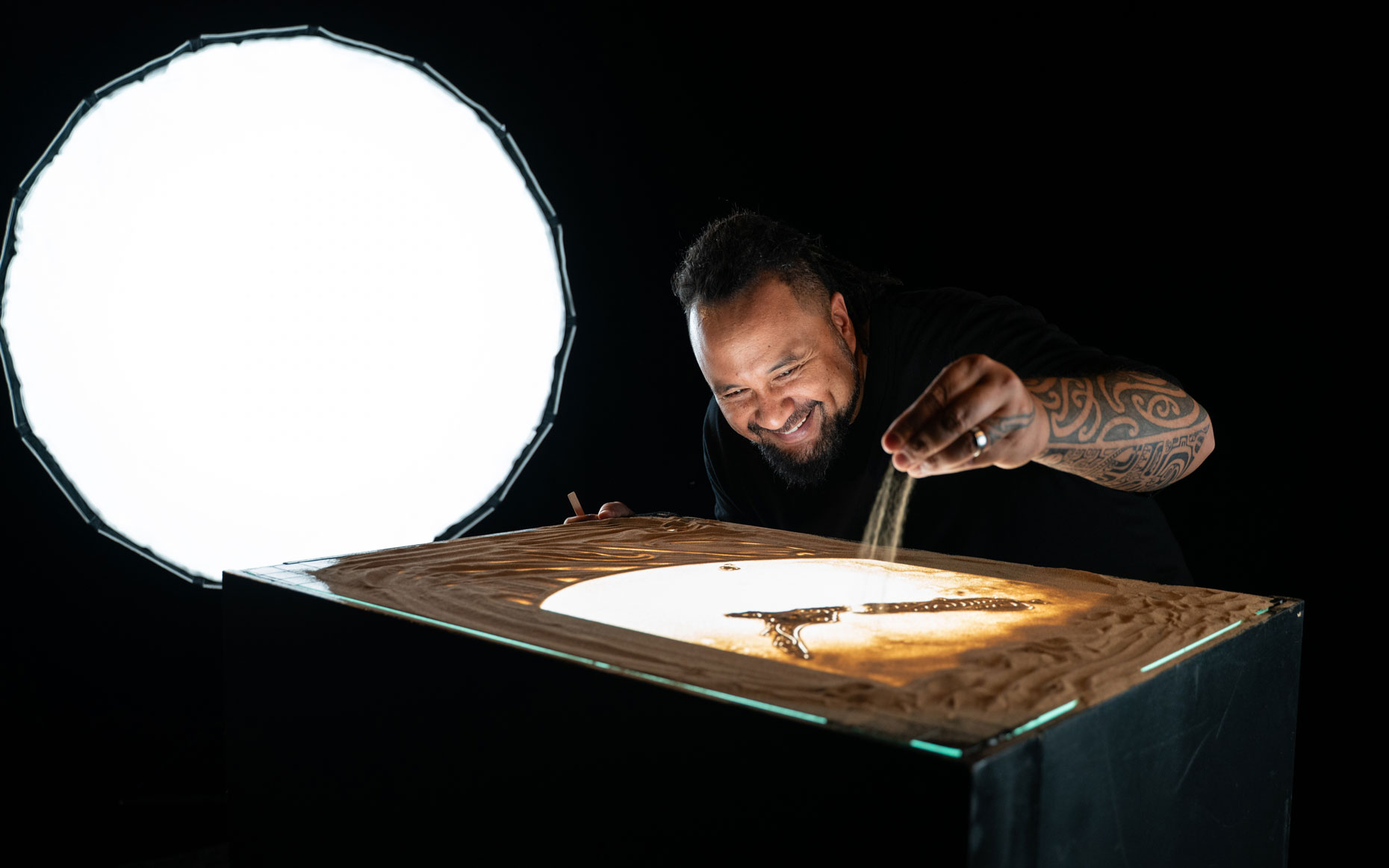 Marcus Winter smiling and sprinkling sand on a lighted sand art table.