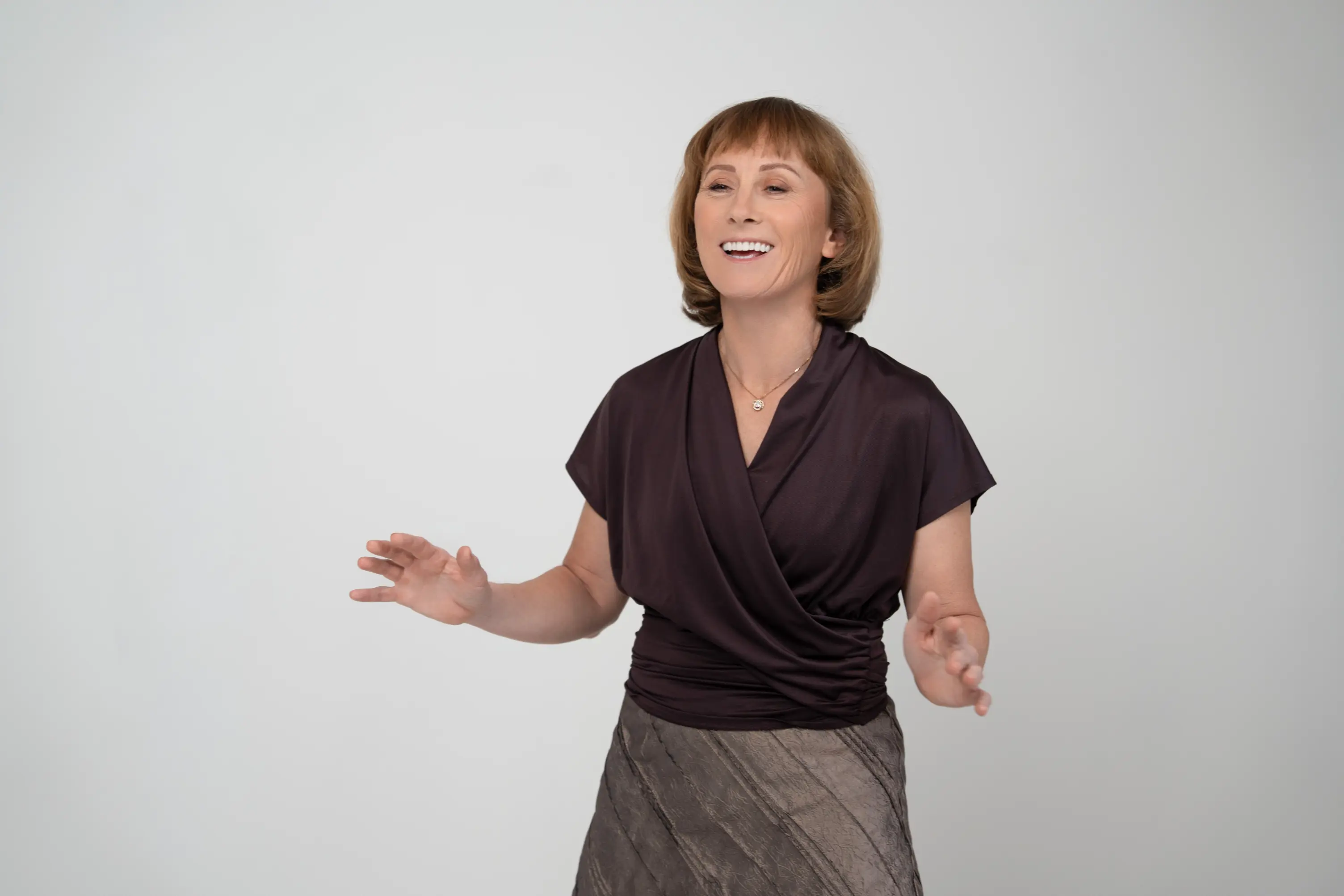 Smiling middle-aged woman with short hair wearing a dark blouse and skirt against a plain background.