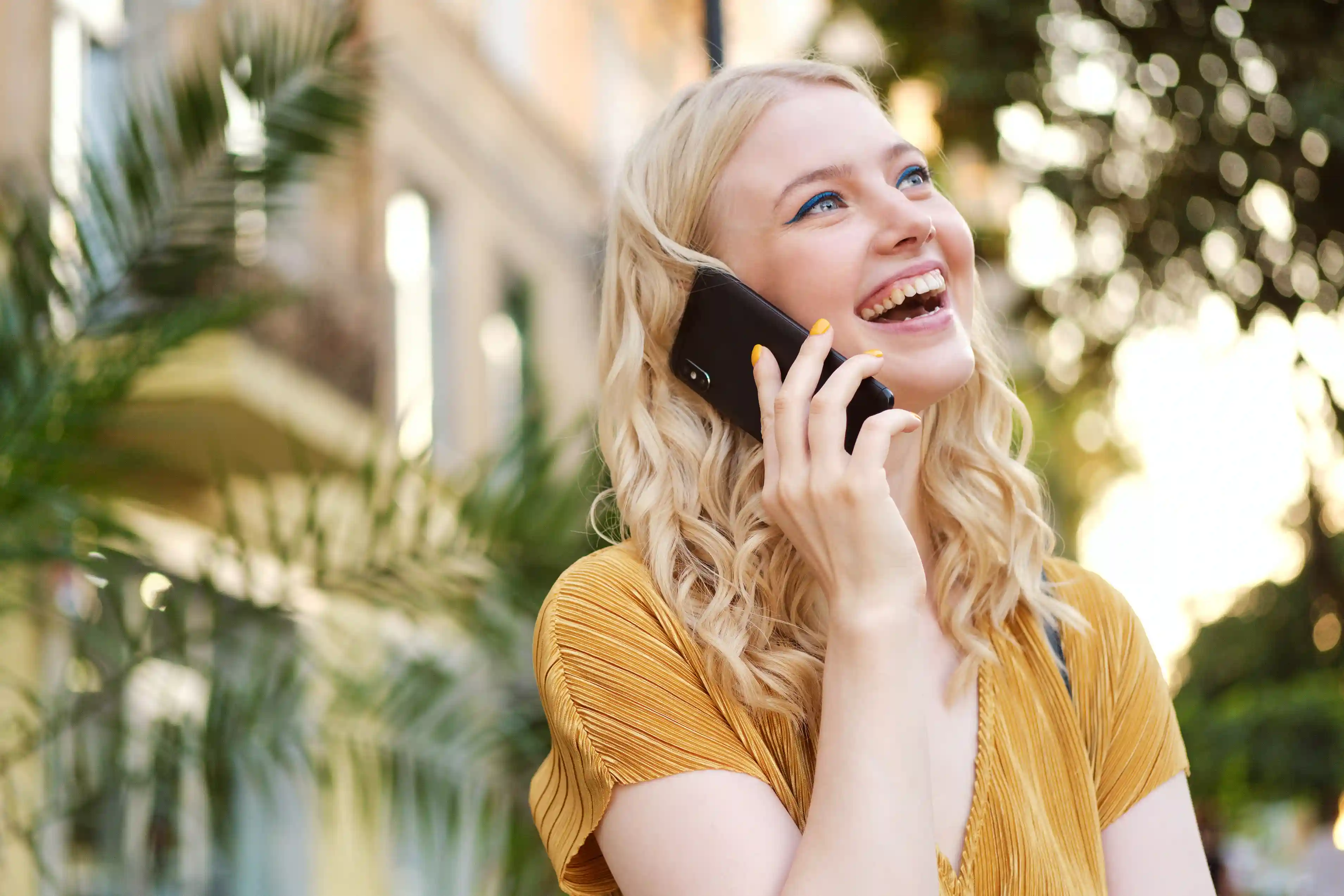 Woman outside a building smiling while talking to someone on her mobile phone