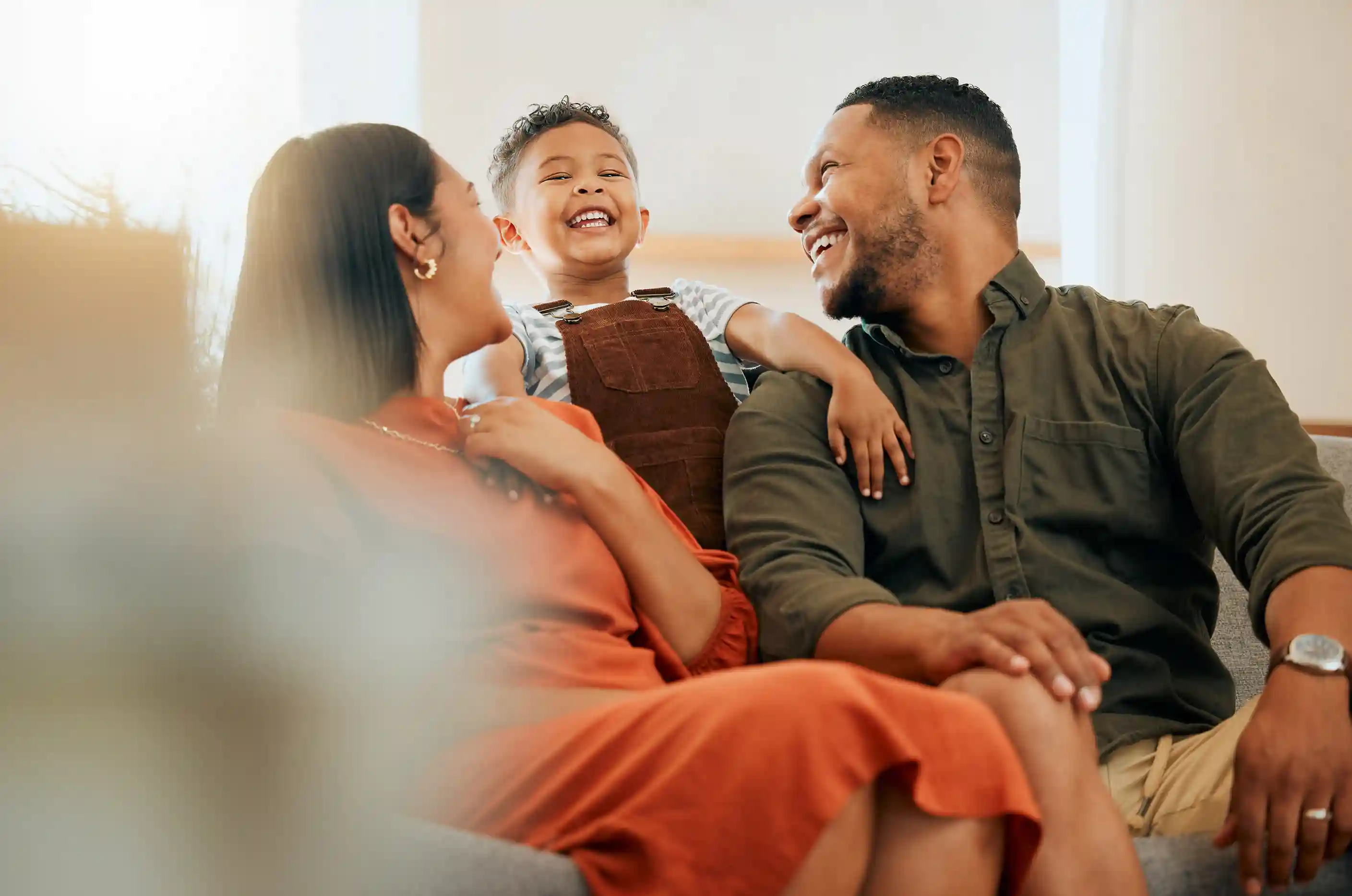 A happy family, smiling and laughing on the couch with their Son on their shoulders