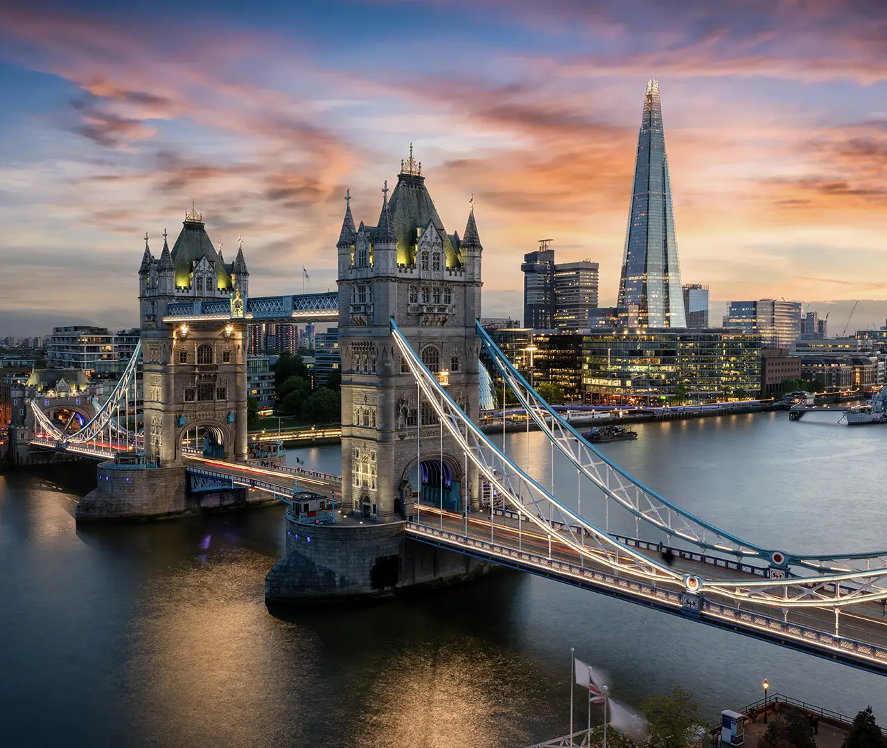 Illuminated Tower Bridge over the Thames at sunset with the Shard and city skyline in the background.