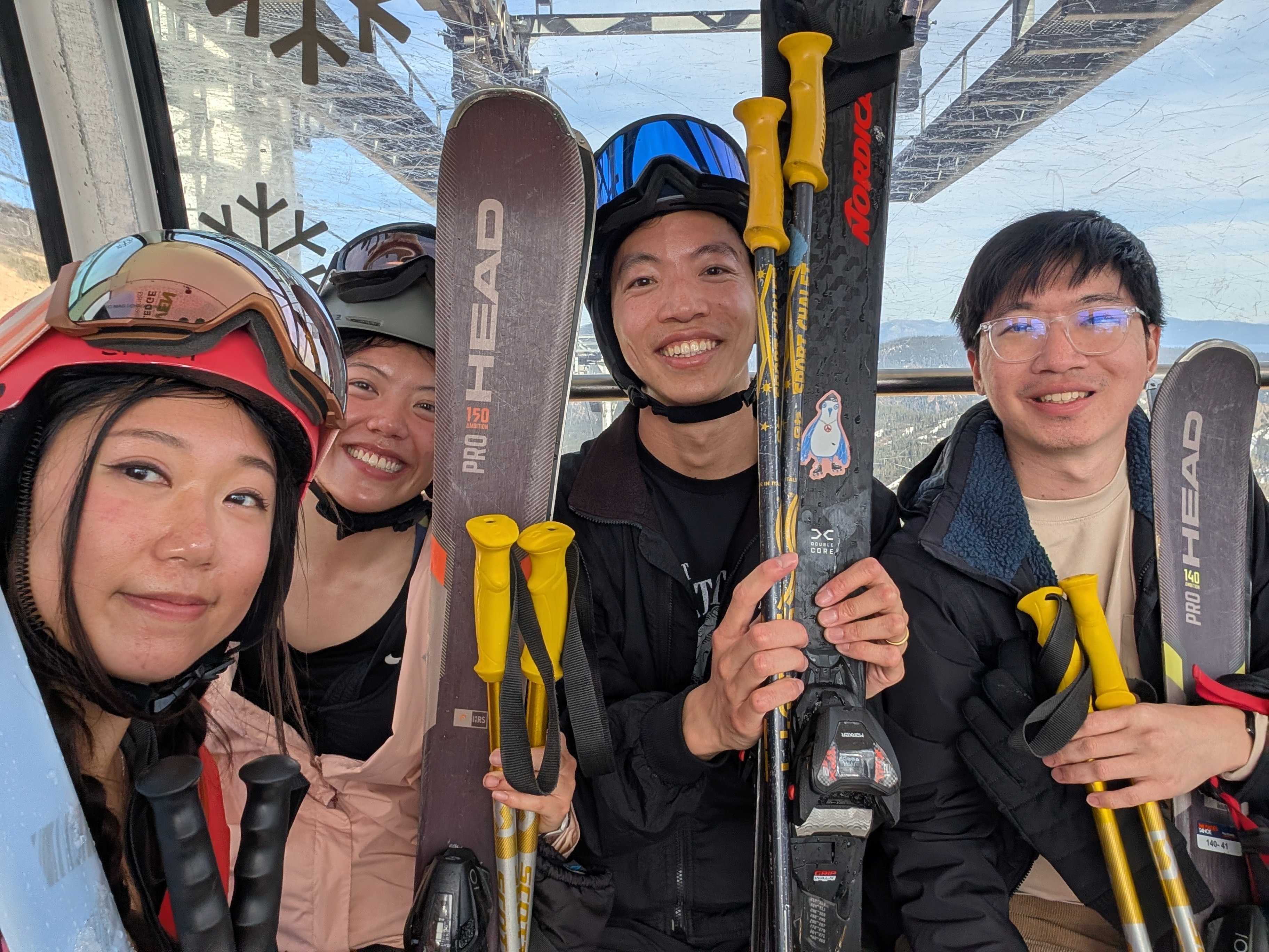 Four Phonic team members with skis and poles inside a mountain gondola.