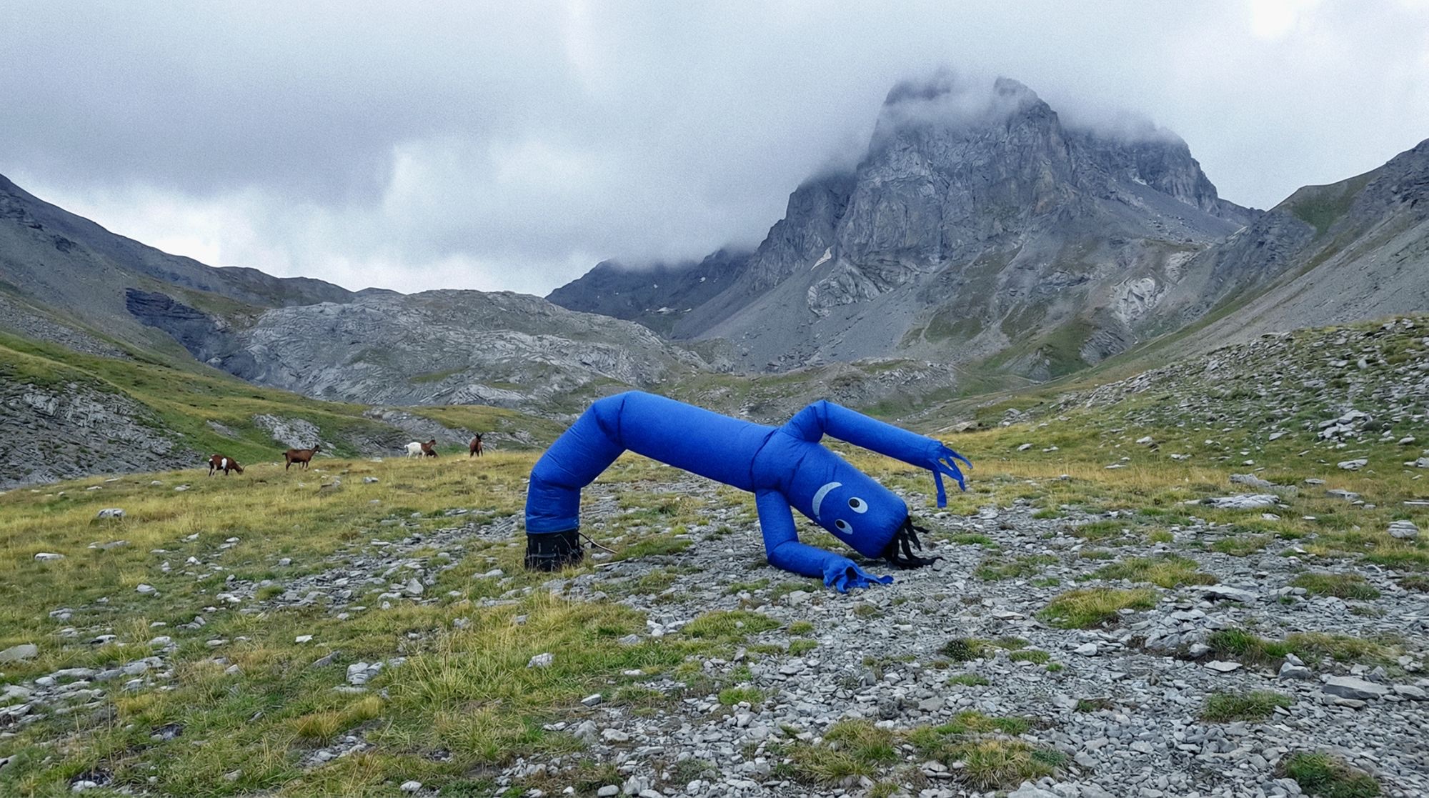 Blue inflatable figure bending over in a mountain landscape