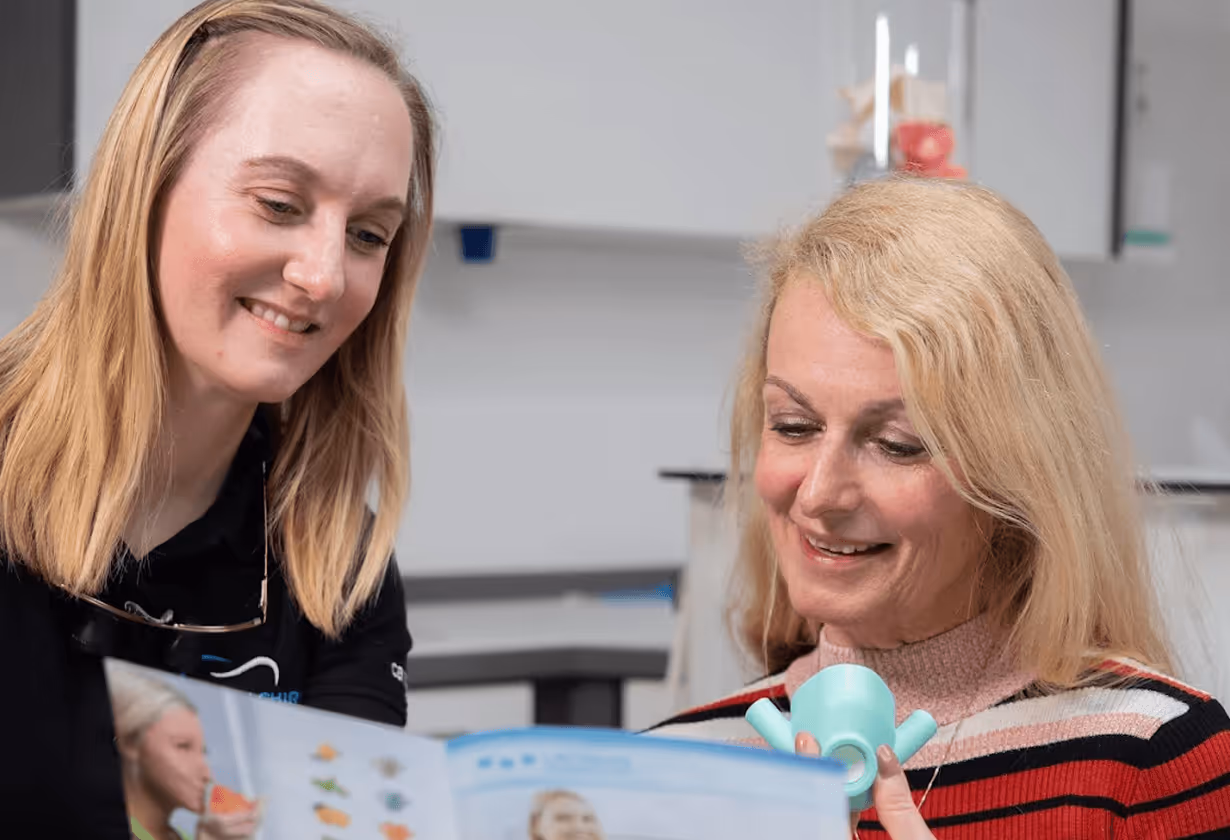 Zwei Frauen in einer Besprechungssituation, lächelnd und ein Broschüren studierend, in einem modernen, hellen Raum.