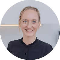 Lächelnde Frau mit blonden Haaren in dunklem Oberteil, Hintergrund minimalistisch gestaltet.