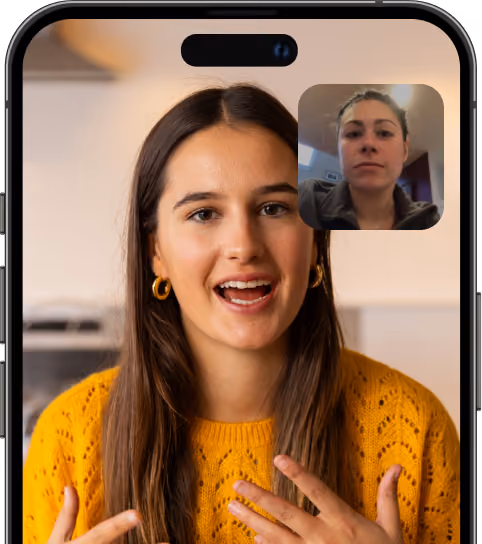 Video call screenshot on a smartphone showing a woman with long brown hair wearing a yellow sweater and gold hoop earrings speaking, with another woman in a smaller inset window appearing serious.