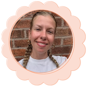 Smiling woman with braided hair and hoop earrings against a brick wall background.
