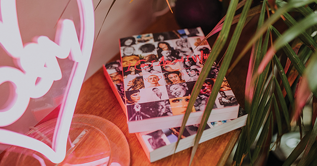 Stack of books with black-and-white faces on the covers beside green plant leaves on a wooden surface.