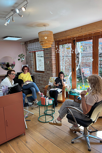 Four women chatting in a cozy room with wooden floors, large windows, and modern furniture.