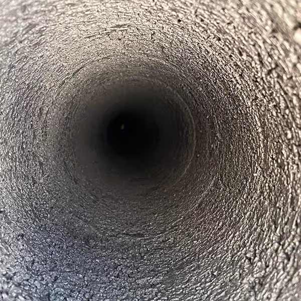 Nærbilde inn i en mørk, teksturert tunnel eller skorstein med ru overflate.