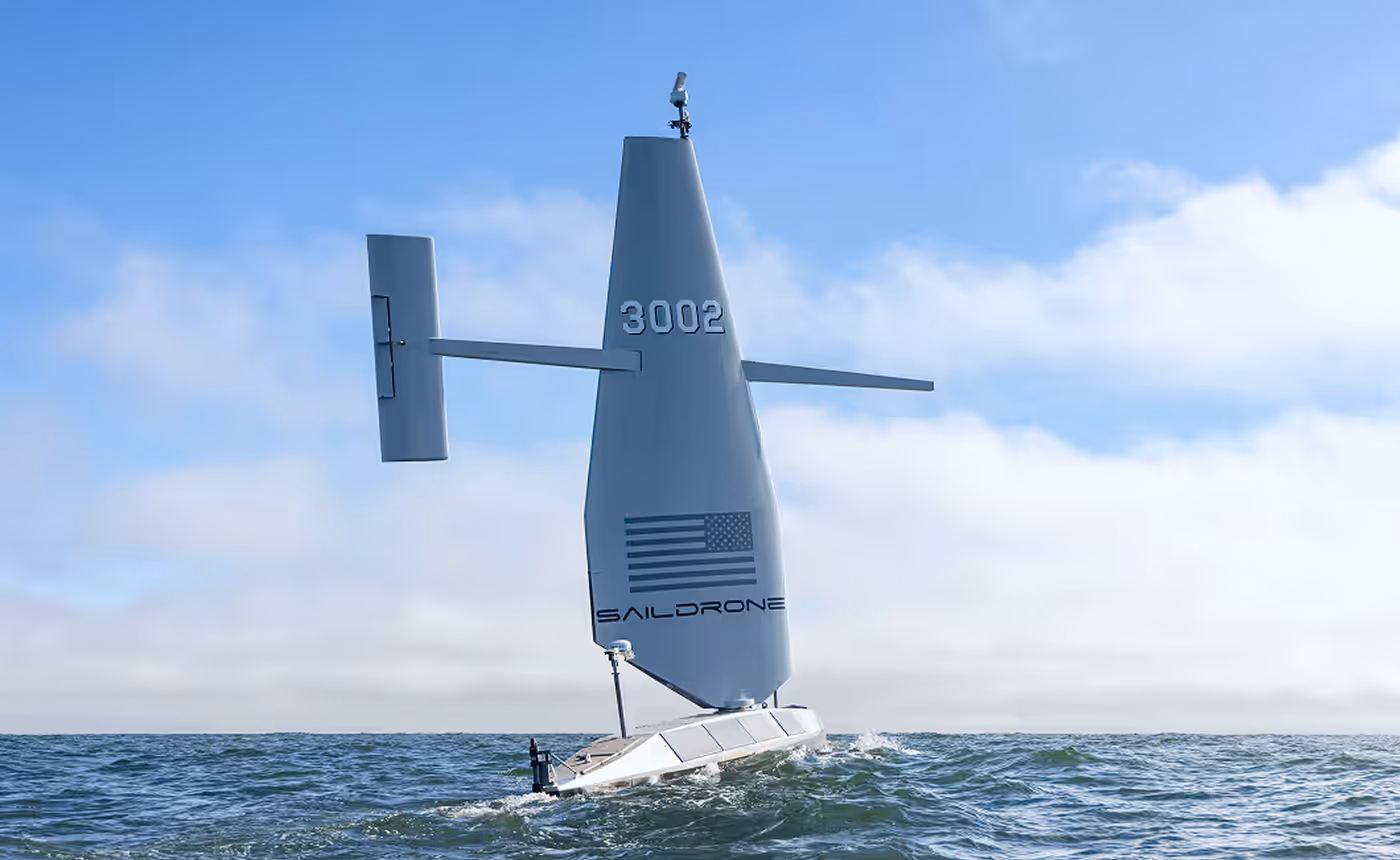 Autonomous Saildrone sailing on ocean waves with clear blue sky and scattered clouds.