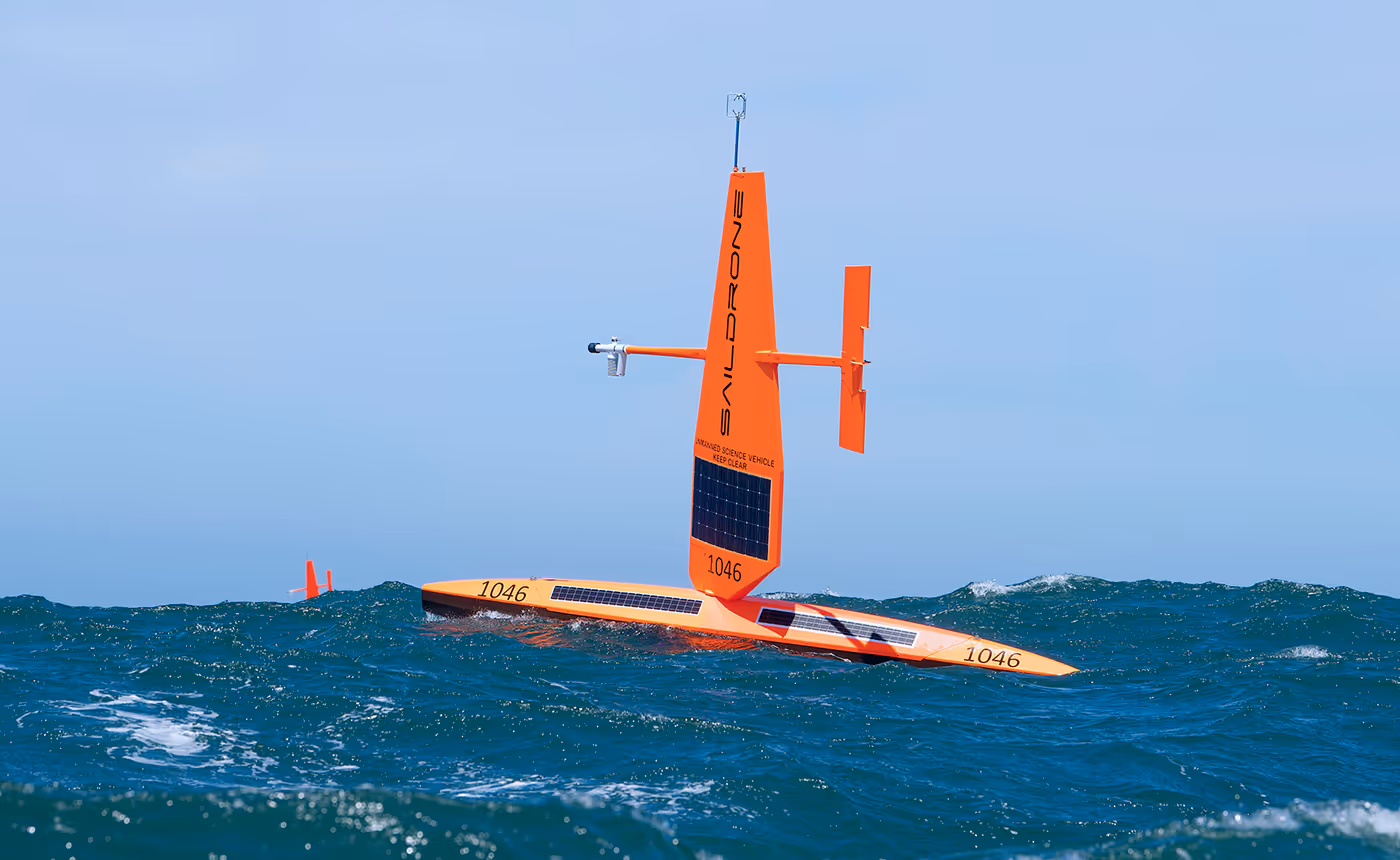 Orange autonomous Saildrone with solar panels floating on wavy ocean under clear sky.