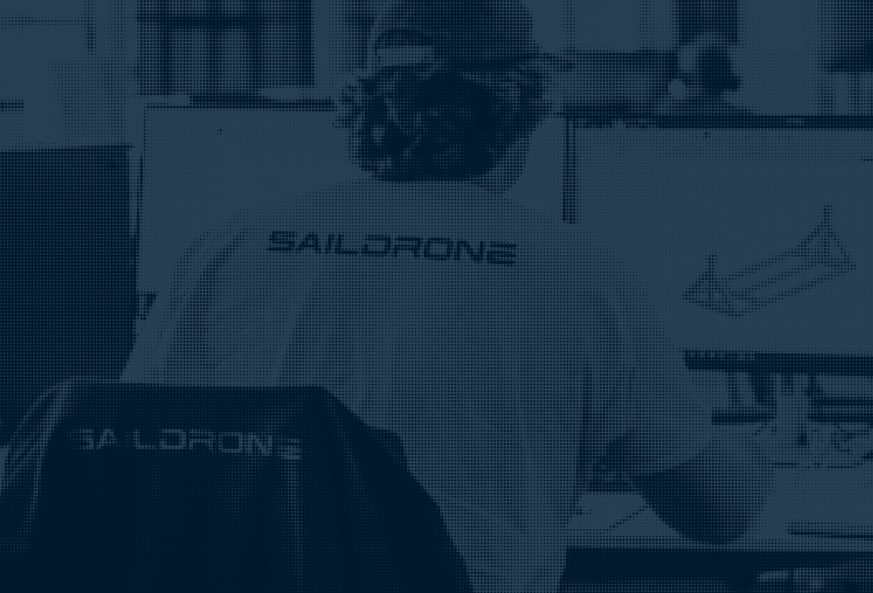 Person wearing a Saildrone shirt, working at a desk with blueprints and a Saildrone model.