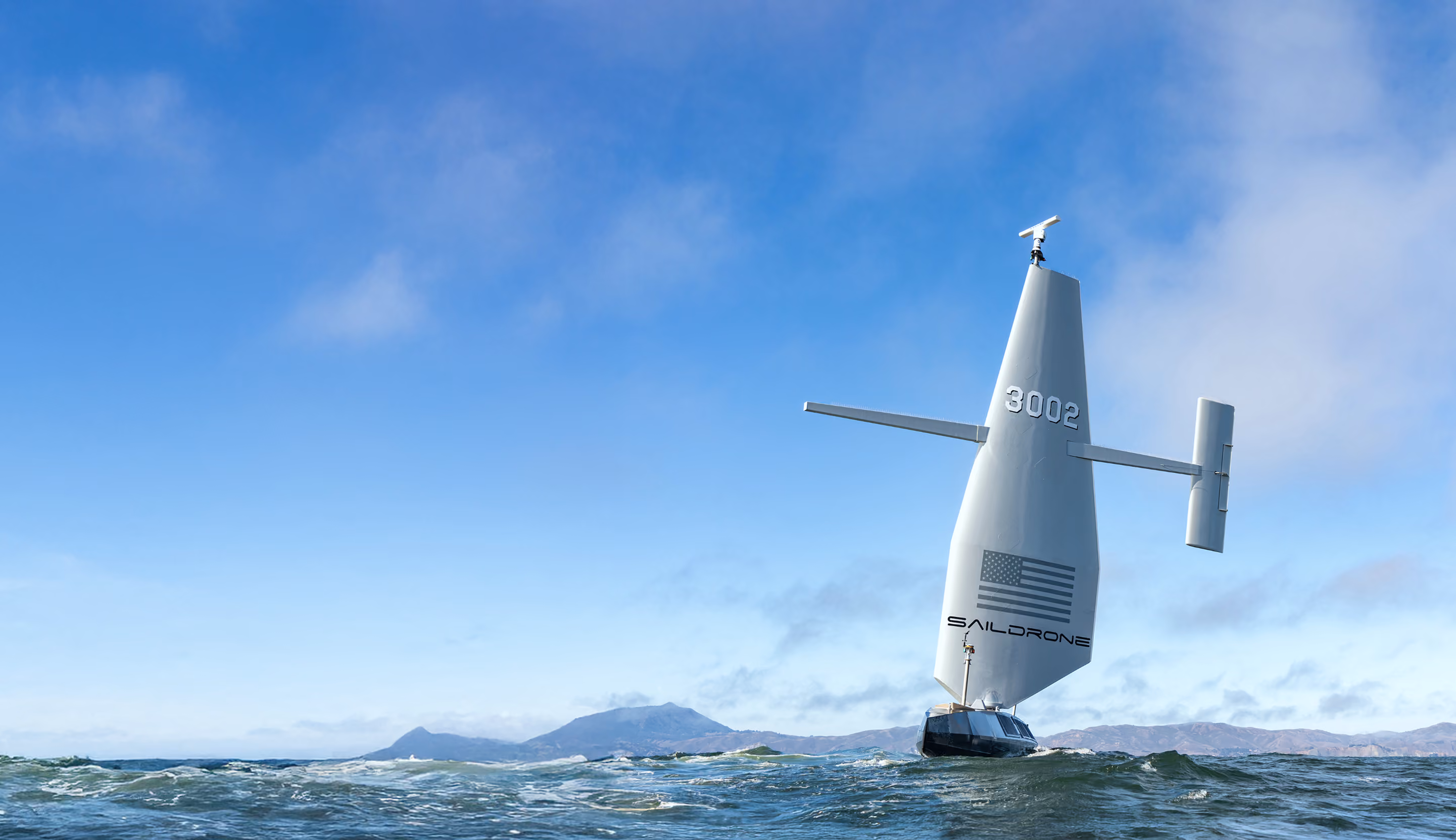 Saildrone autonomous vessel on water with numbered sail and American flag under clear blue sky.