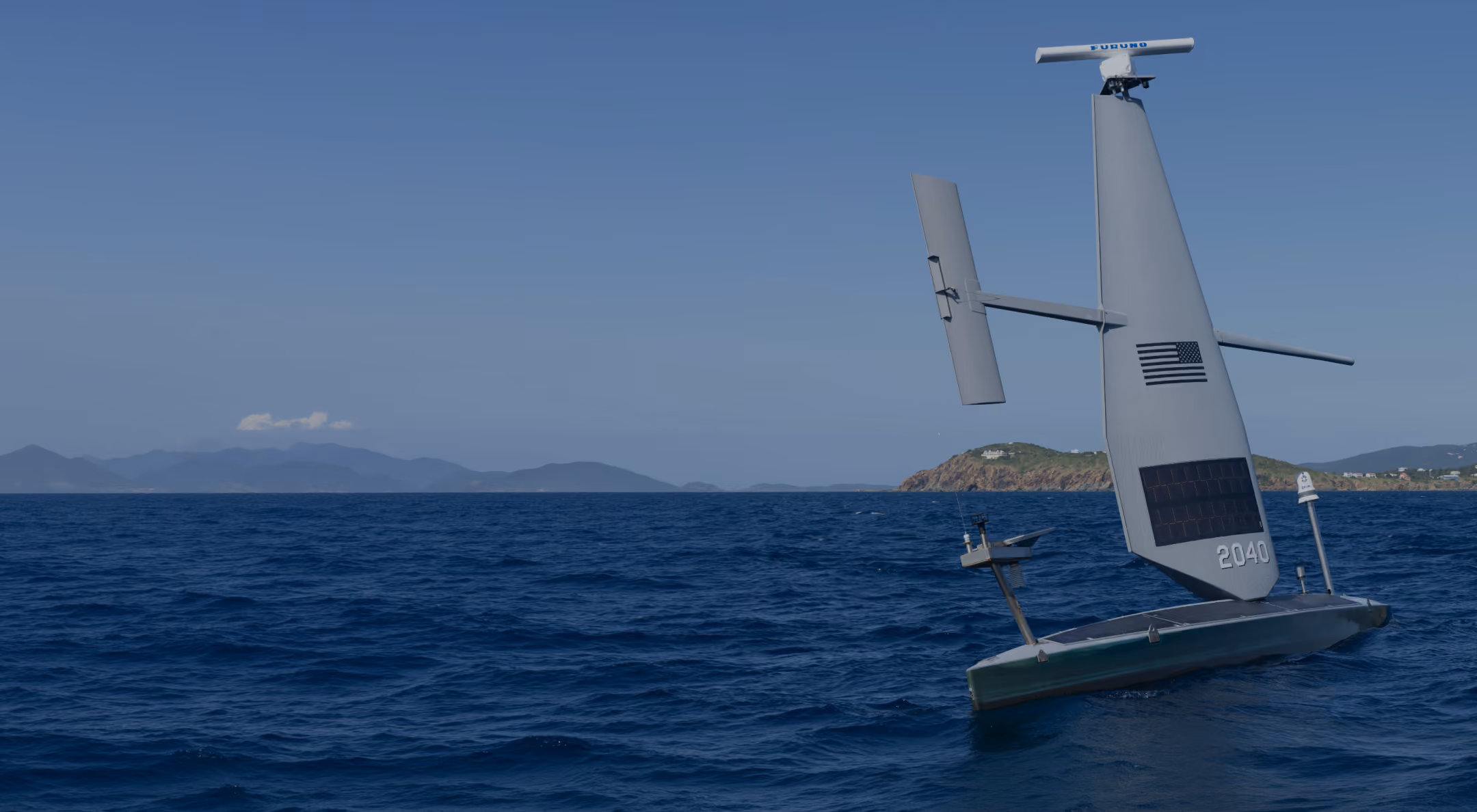 Autonomous Saildrone with solar panels and US flag sailing on blue ocean near mountainous coast.
