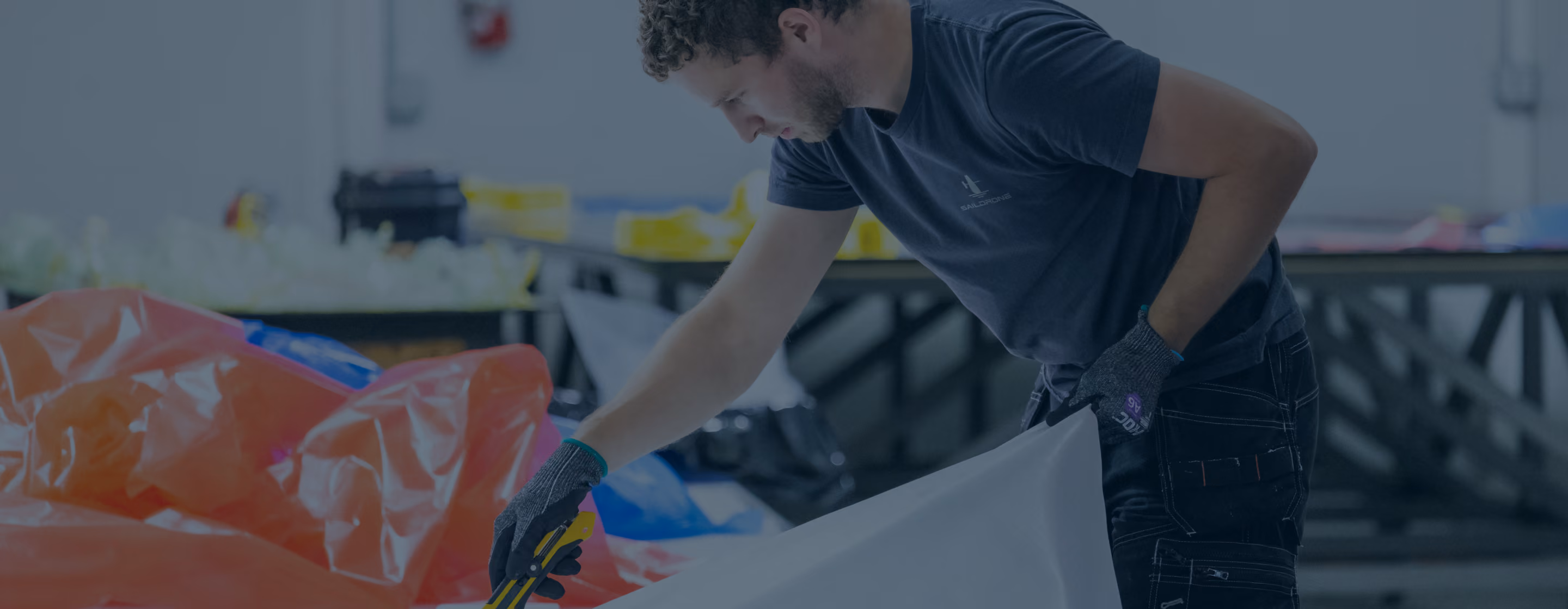Man in gloves cutting large white sheet with yellow utility knife in a workshop.