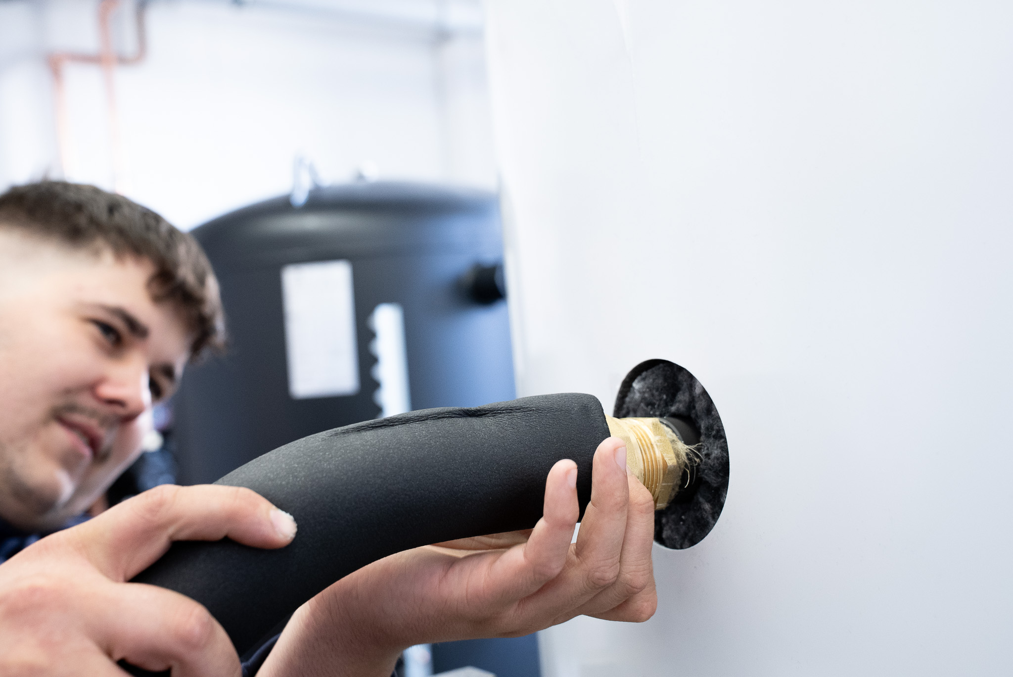 Techniker montiert Isolierung an einem Rohranschluss an einer weißen Wand.