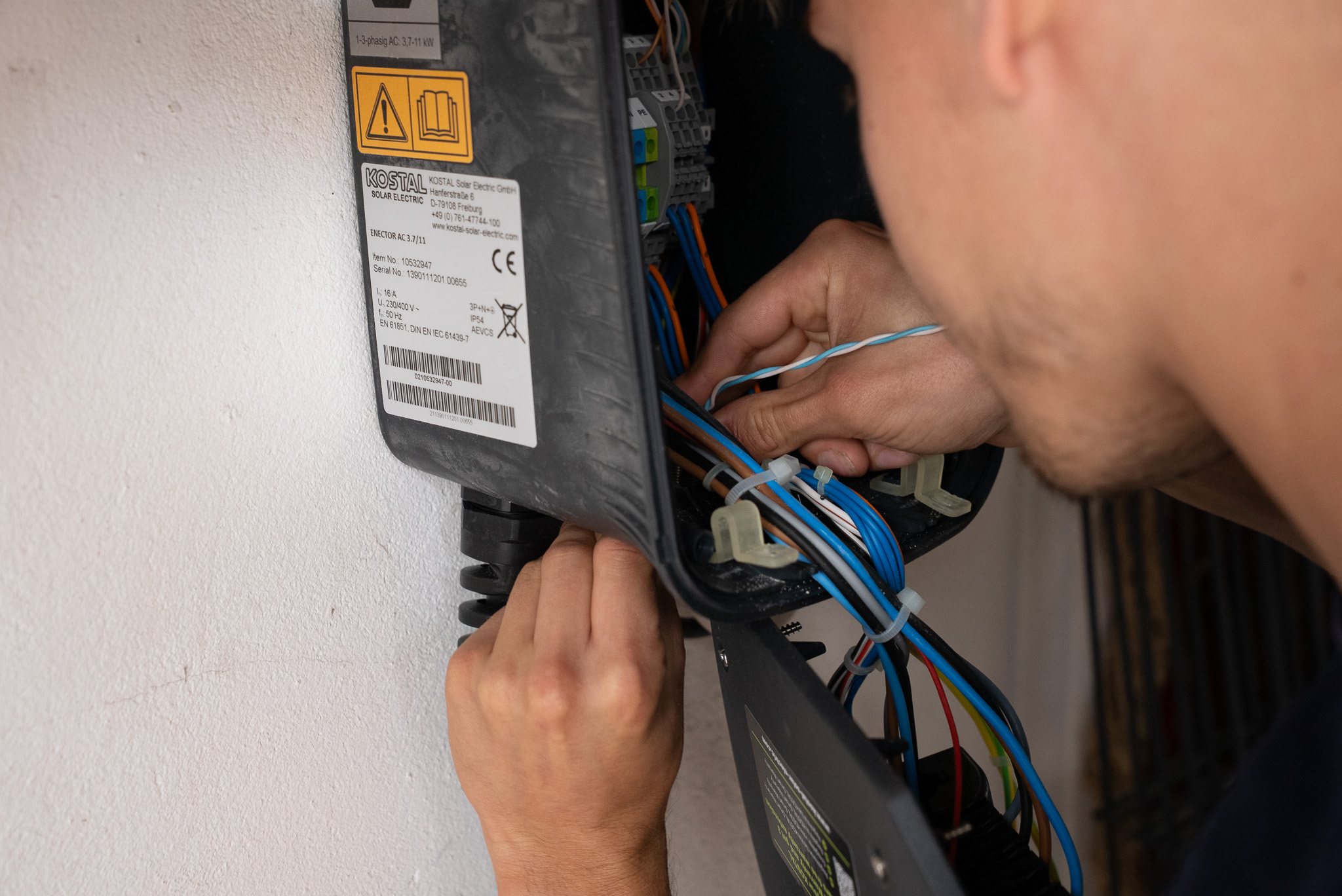 Person arbeitet an elektrischen Drähten in einem geöffneten KOSTAL Solar Electric Gehäuse.