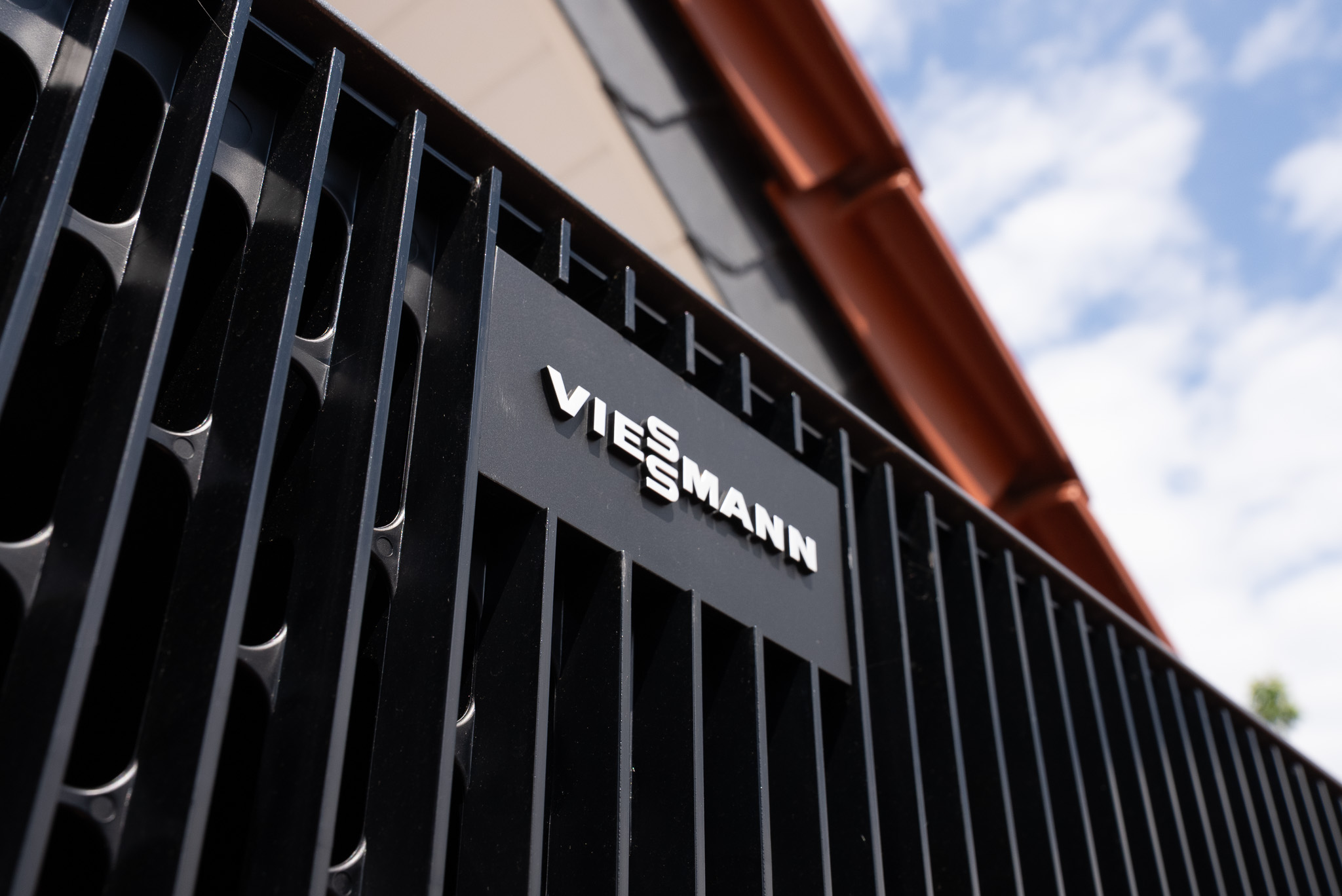 Graue Viessmann-Wärmepumpe an einer beige verputzten Hauswand im Sonnenschein.