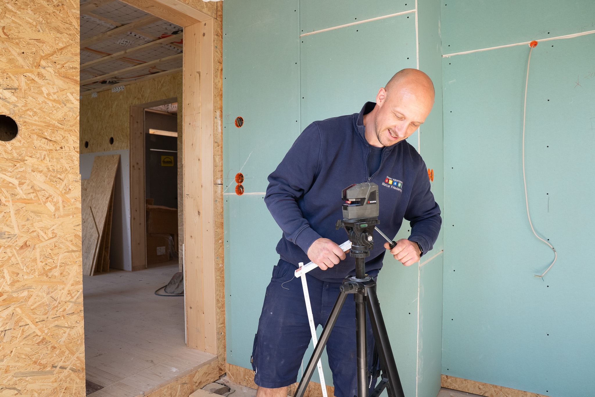 Handwerker richtet Lasergerät auf Stativ in einem im Bau befindlichen Raum aus.