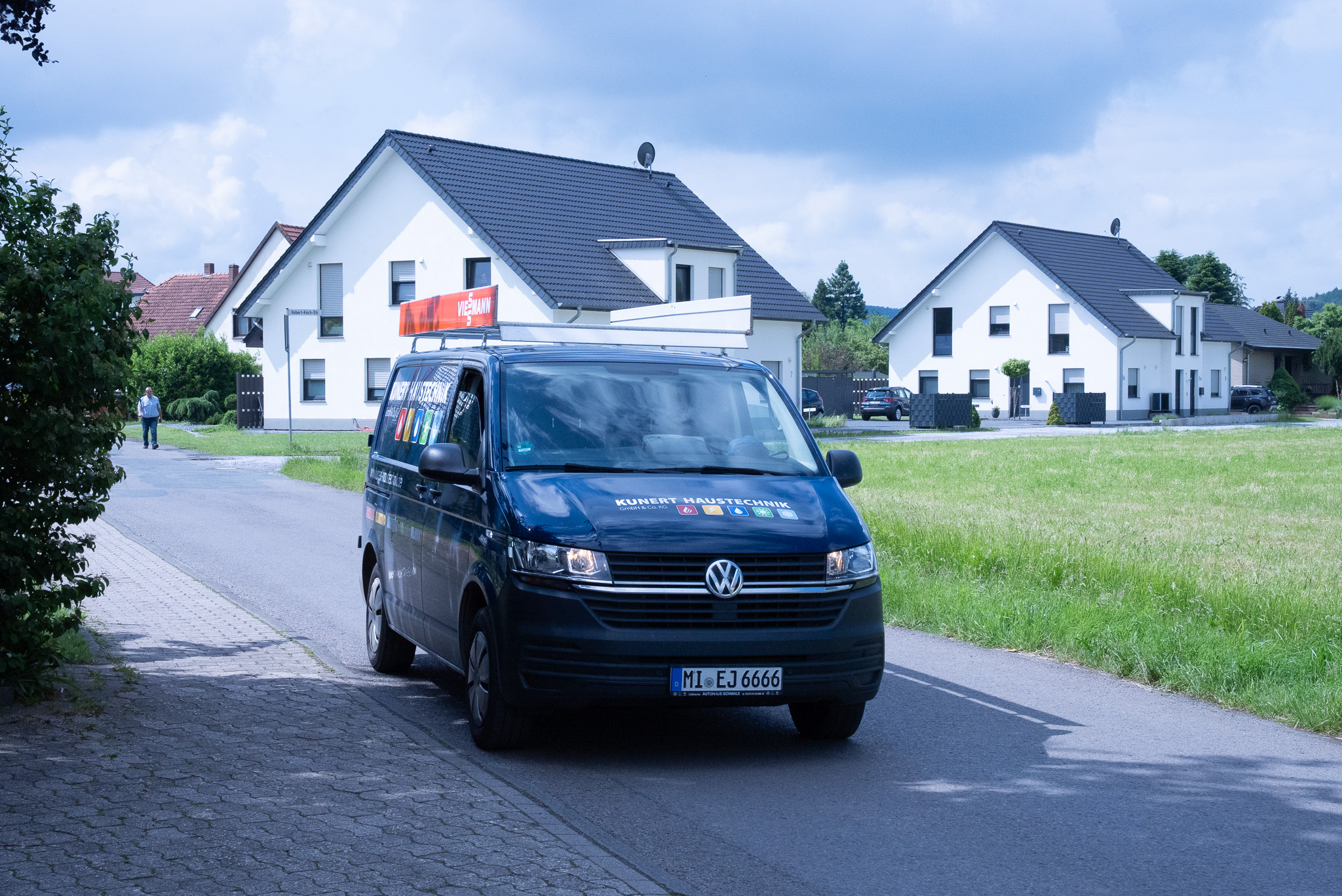 Dunkelblauer Volkswagen Transporter mit Firmenwerbung parkt an einer Straße in einem Wohngebiet.