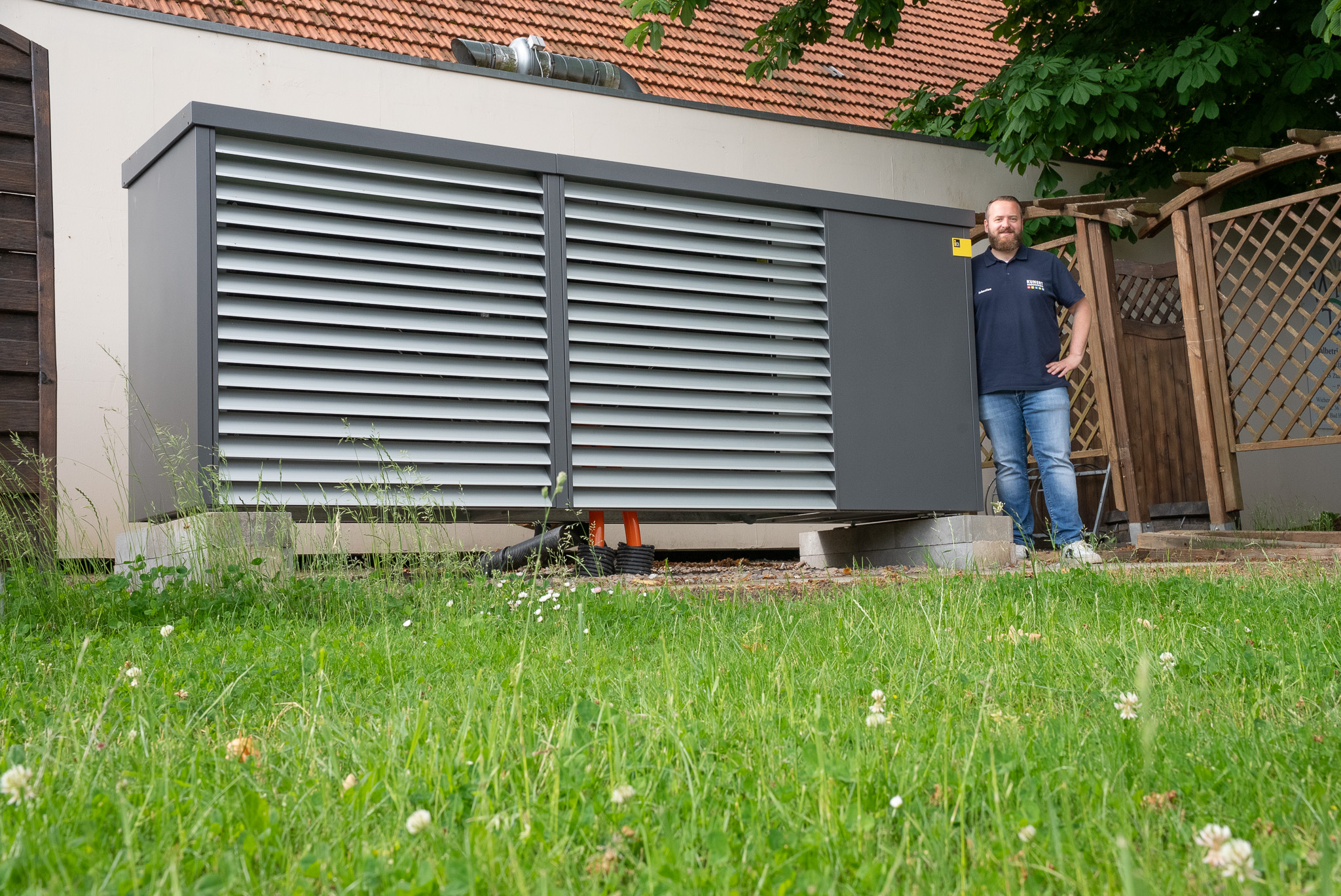 Graue Viessmann-Wärmepumpe an einer beige verputzten Hauswand im Sonnenschein.
