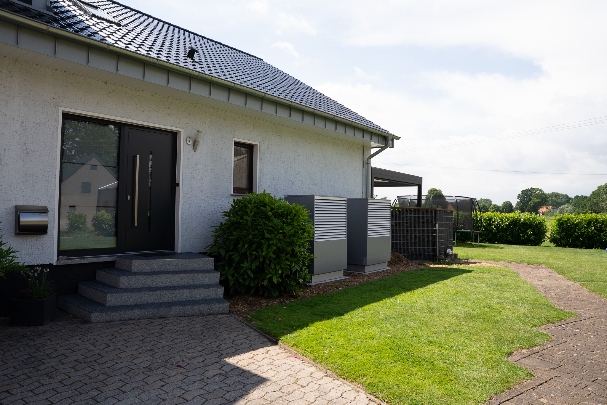Eingang eines weißen Hauses mit schwarzer Tür, Stufen und gepflegtem Rasen im Sonnenschein.