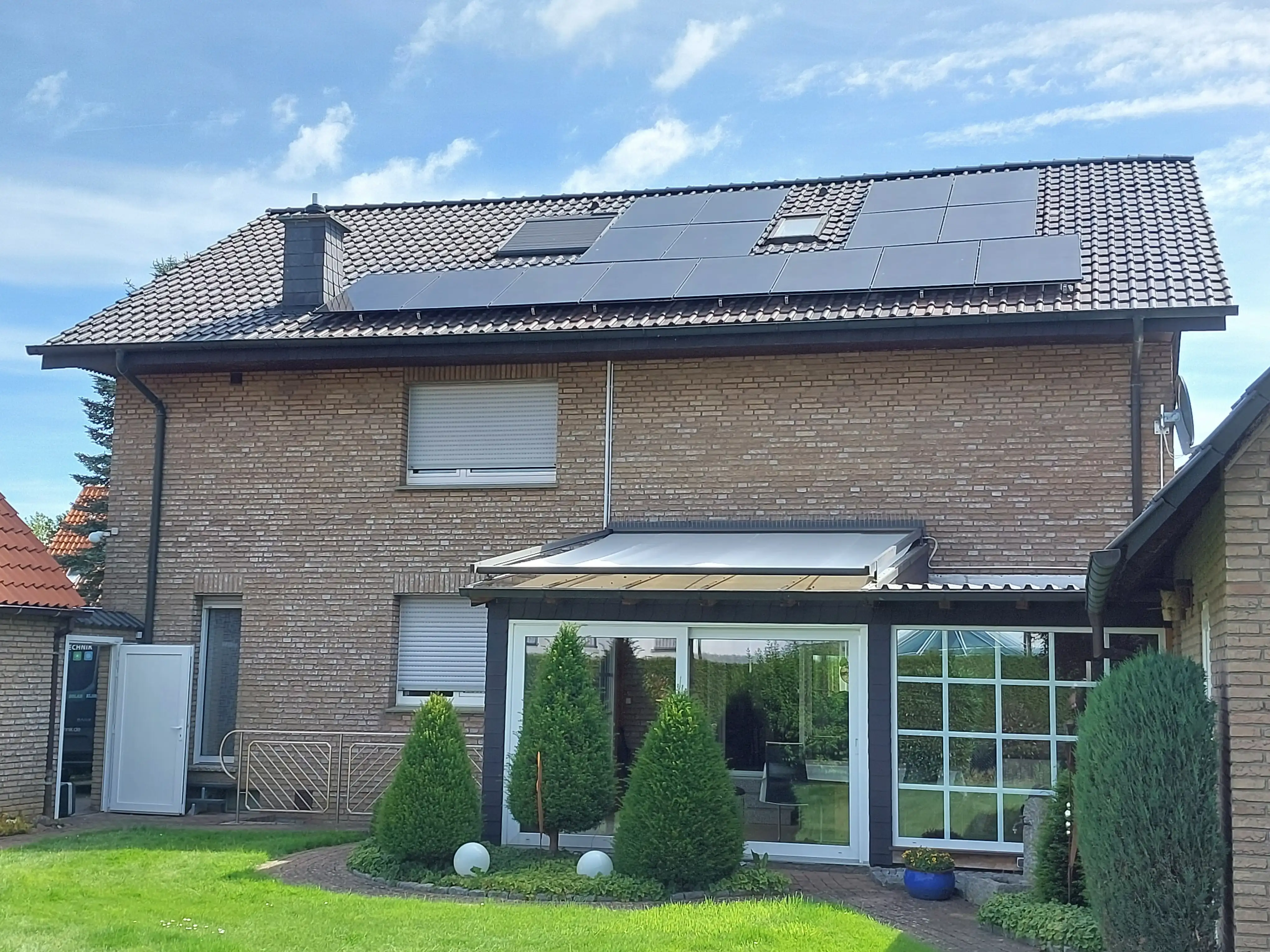 Zweistöckiges Haus mit Solaranlage auf dem Dach, kleinem Garten und verglaster Terrasse.