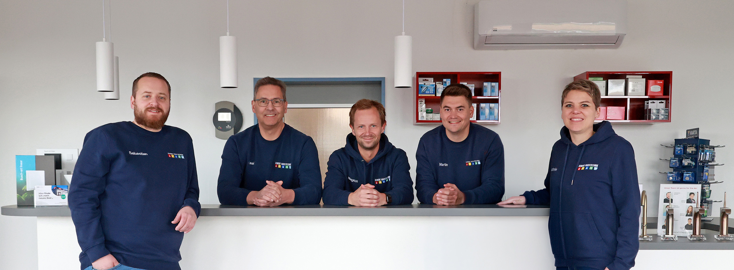 Fünf Personen in blauen Pullovern mit Logos stehen lächelnd an einer Theke im Büro.