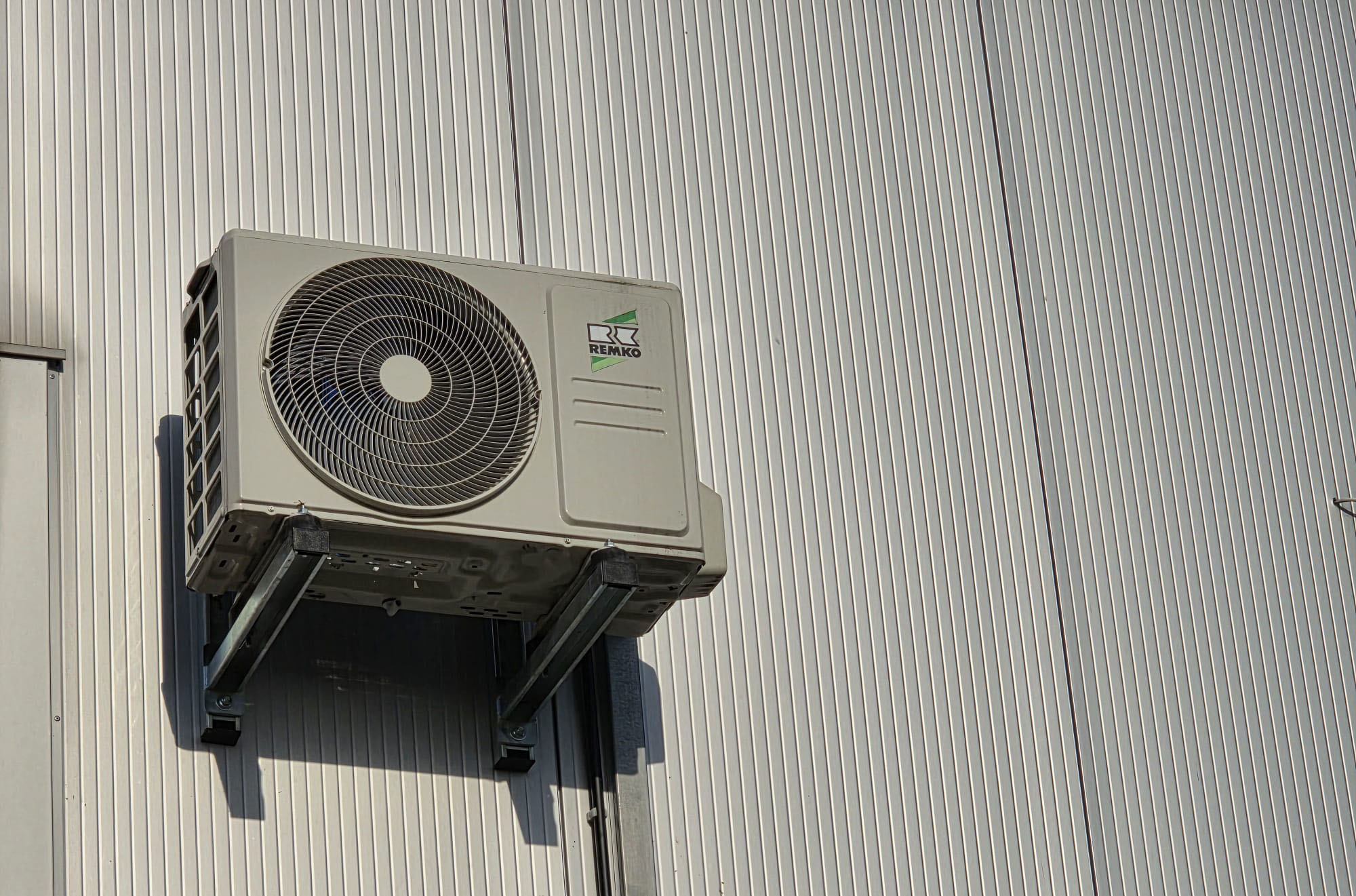 Außenluftgerät einer Klimaanlage an einer grauen Gebäudeaußenwand montiert.