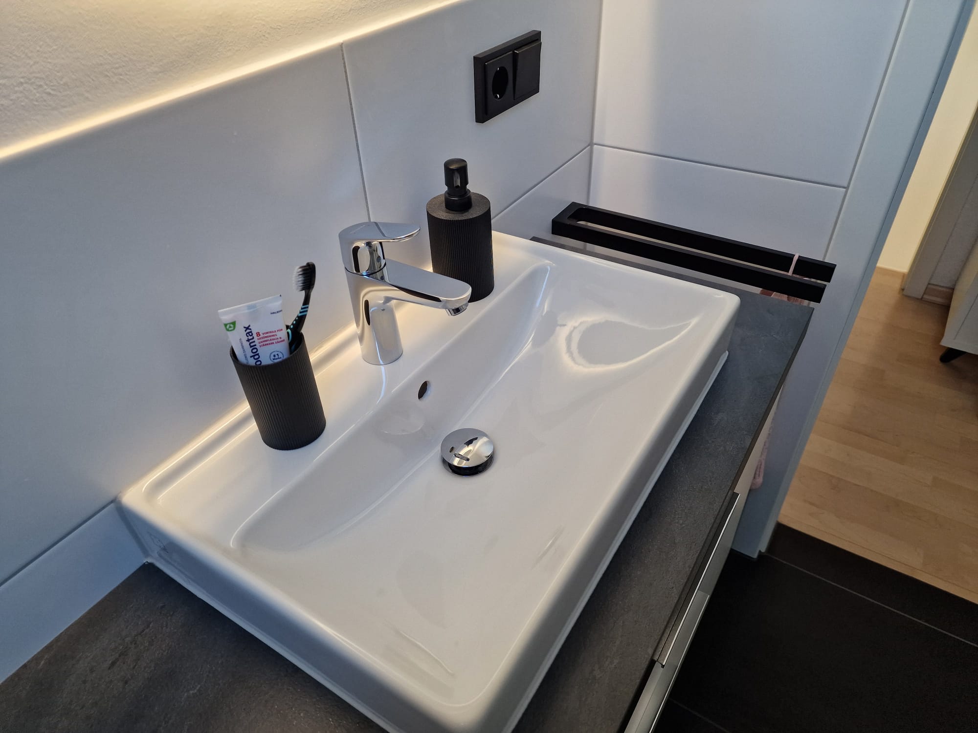 Badezimmerwaschbecken mit Zahnbürste, Zahnpasta und Seifenspender auf der Arbeitsplatte.