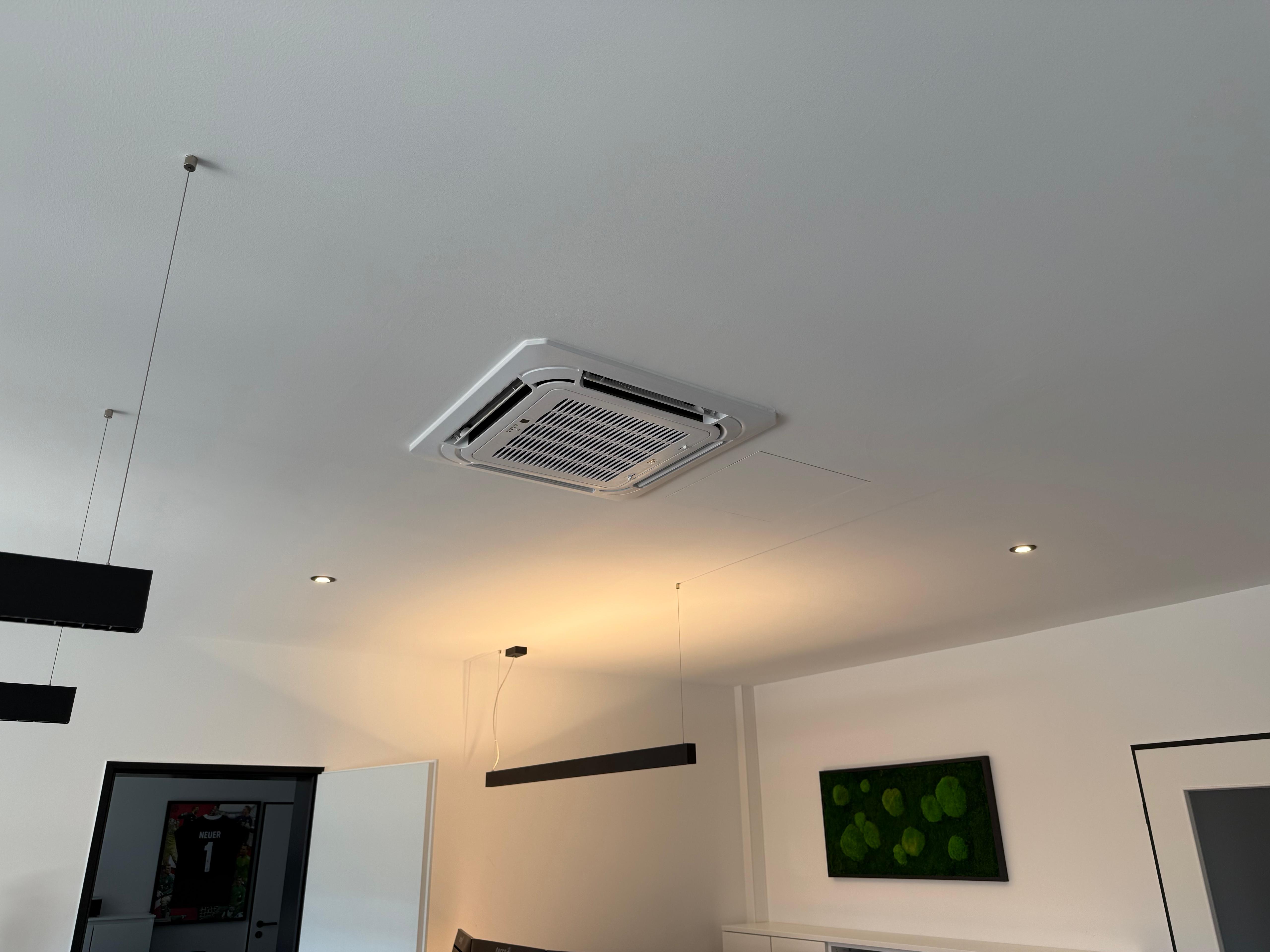 Moderne weiße Zimmerdecke mit eingebauter Klimaanlage, schwarzen Hängeleuchten und Wandbild mit grünen Blättern.