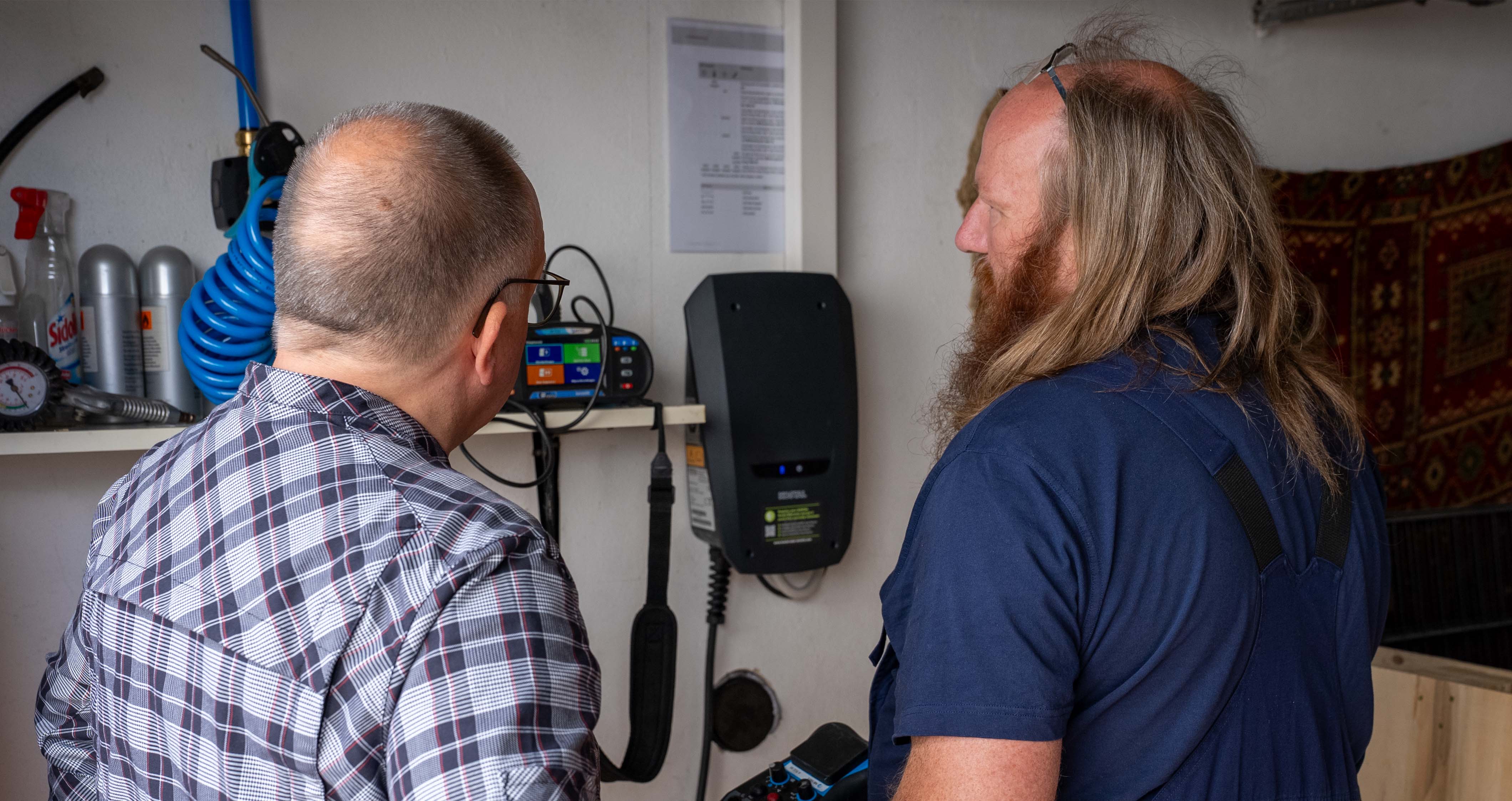 Zwei Männer begutachten ein montiertes elektronisches Gerät an der Wand in einem Arbeitsraum.